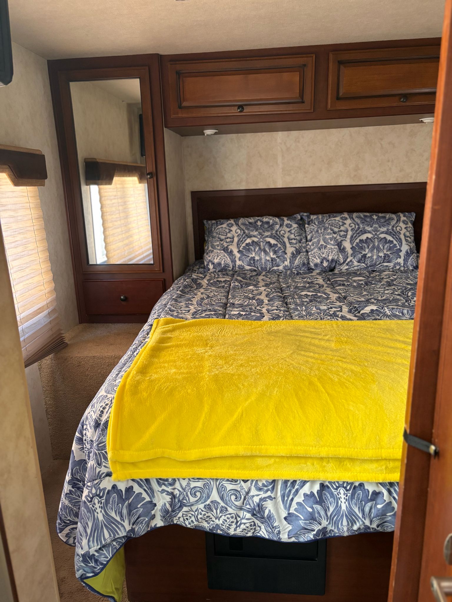 Inside an RV rental: a compact bedroom with blue & white patterned bedding, yellow blanket, wooden cabinets & mirror.. Jamboree Sport 2010