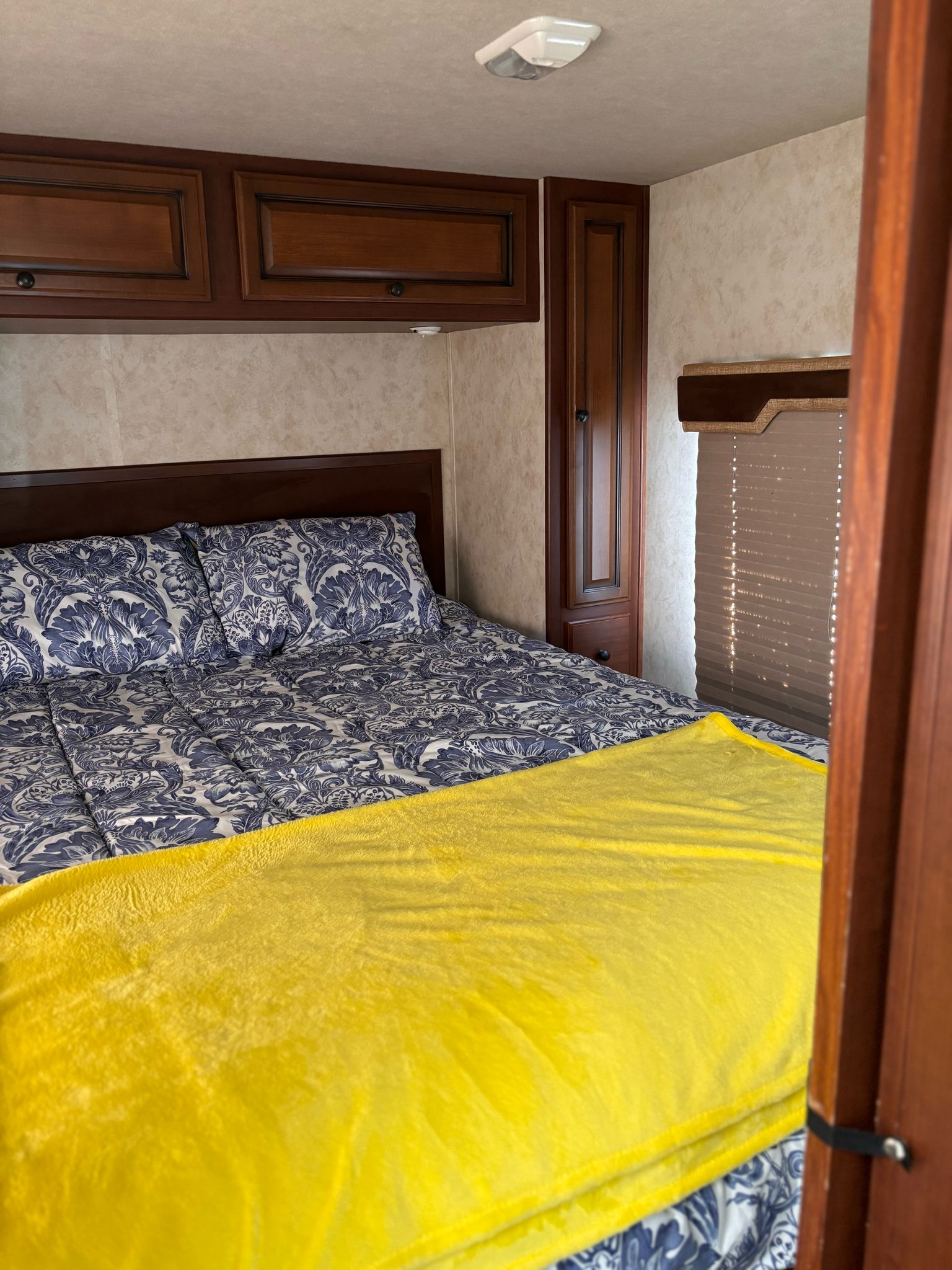 Cozy RV rental bedroom with patterned bed, bright yellow blanket, and ample wooden cabinetry.. Jamboree Sport 2010