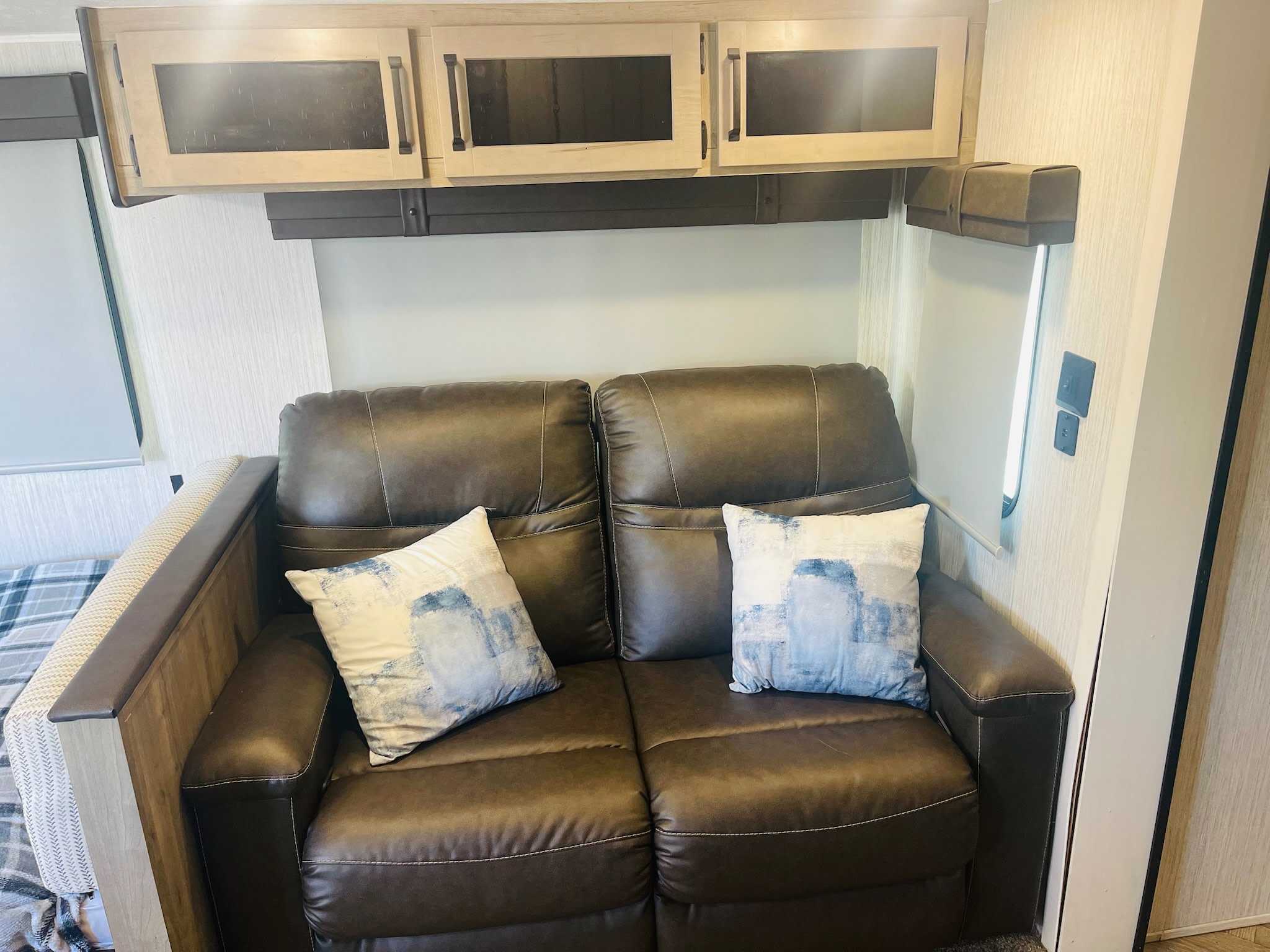 Cozy RV rental interior featuring a comfy brown leather sofa, decorative pillows, and ample overhead storage cabinets.. Forest River Palomino Puma 2022