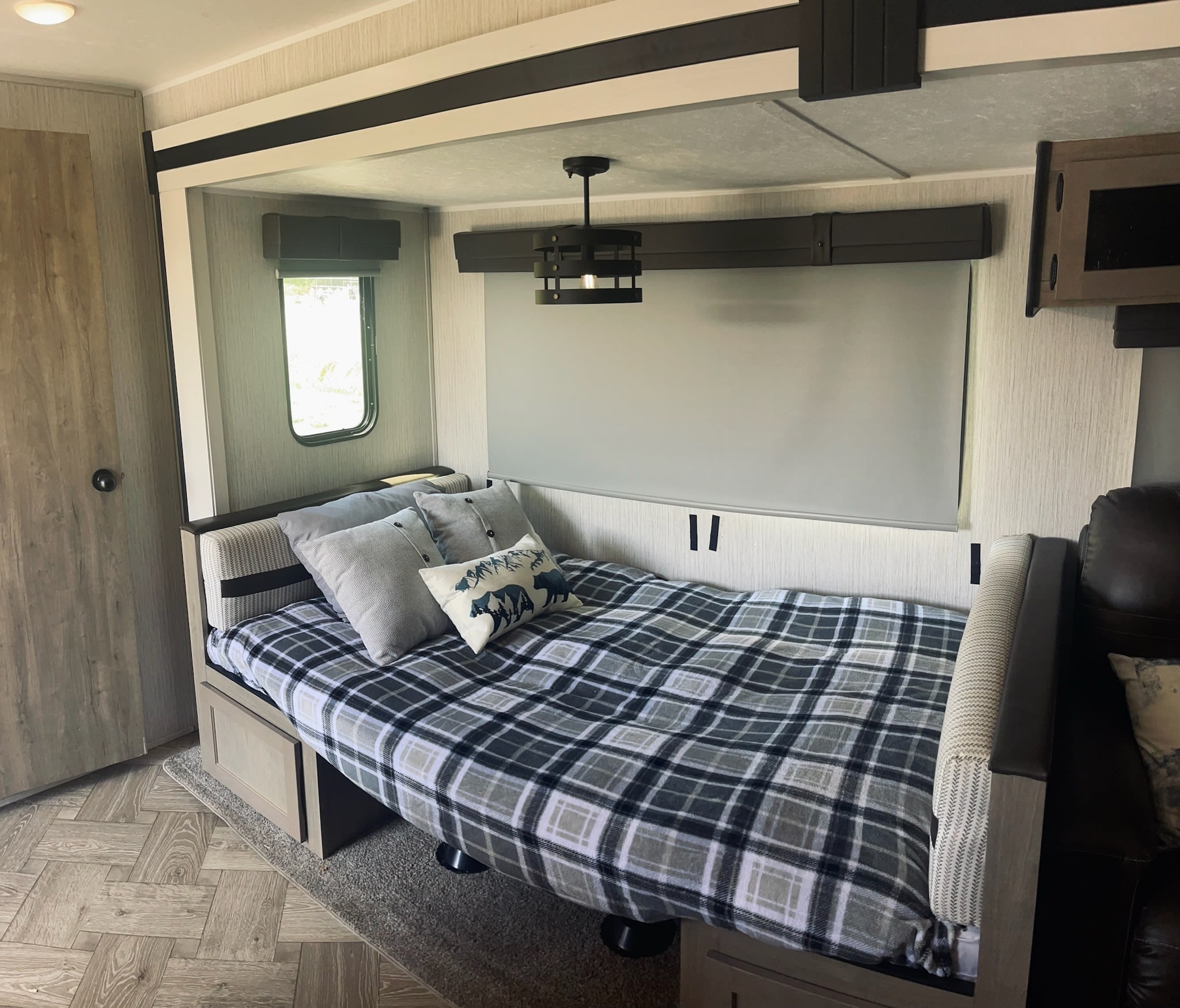 Explore a cozy RV rental bedroom: a comfortable plaid bed, natural light from the window, and stylish wood-look flooring.. Forest River Palomino Puma 2022