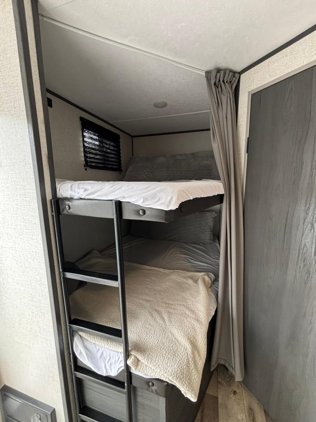 Inside an RV rental, two bunk beds feature a black ladder, window blinds, and a gray privacy curtain for compact, cozy sleeping.. Aspen Trail Aspen Trail Trailer 2022