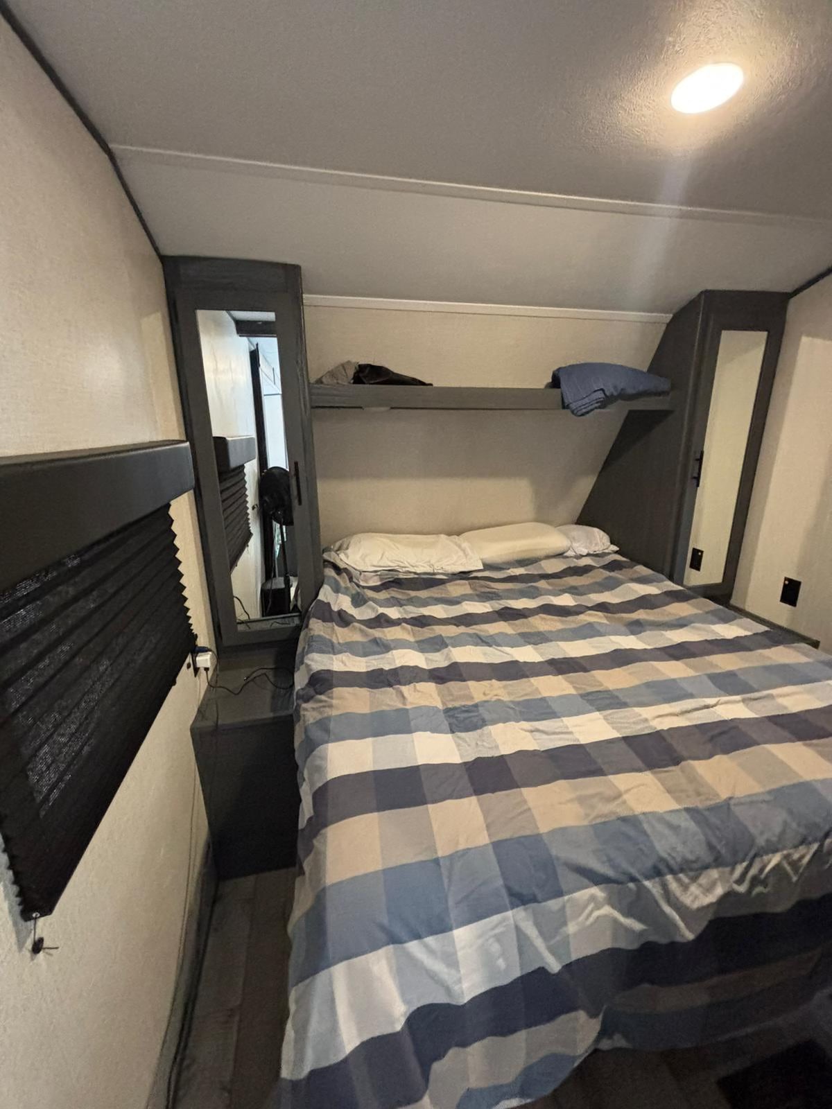 RV rental bedroom: a cozy space with a plaid bed, built-in mirrored cabinet, shelf, and window.. Aspen Trail Aspen Trail Trailer 2022