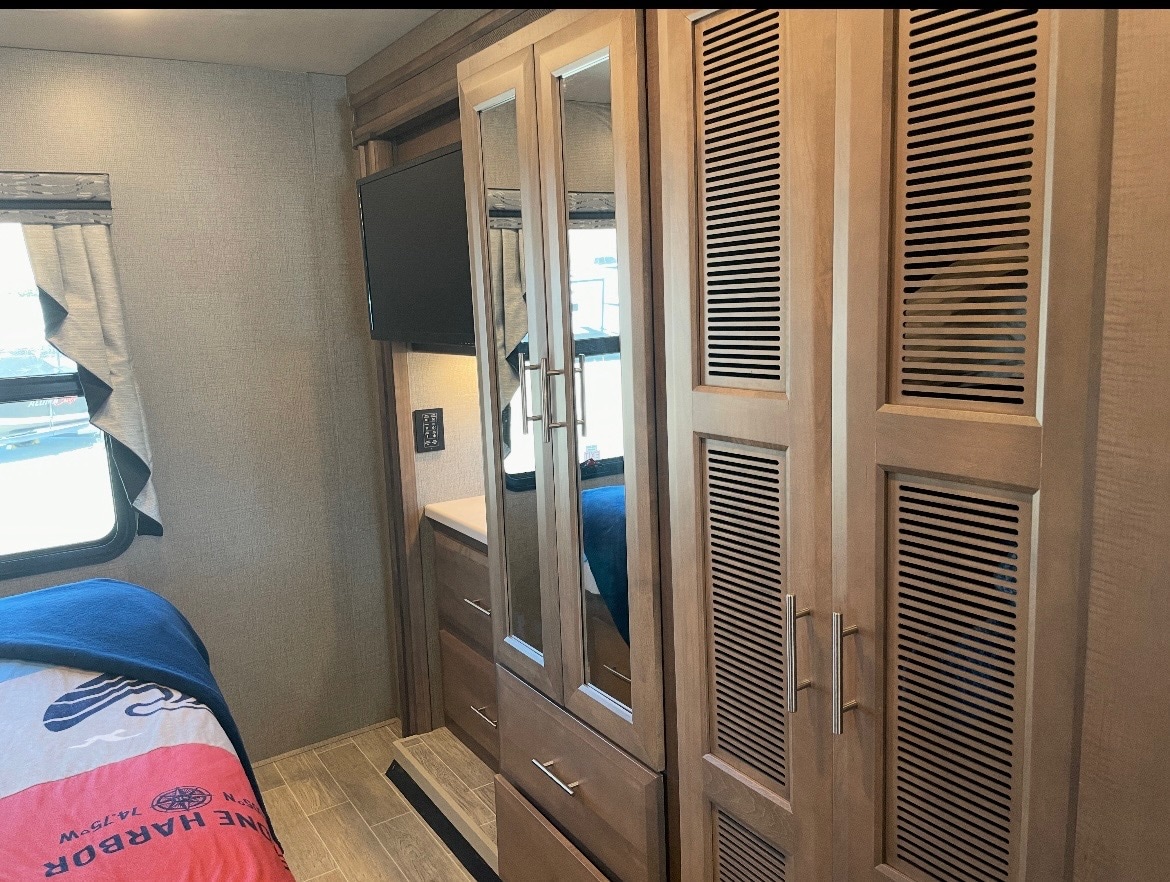 An RV rental's cozy bedroom features a bed, mounted TV, and built-in mirrored & louvered closet storage.. Mirimar 34.8 2022