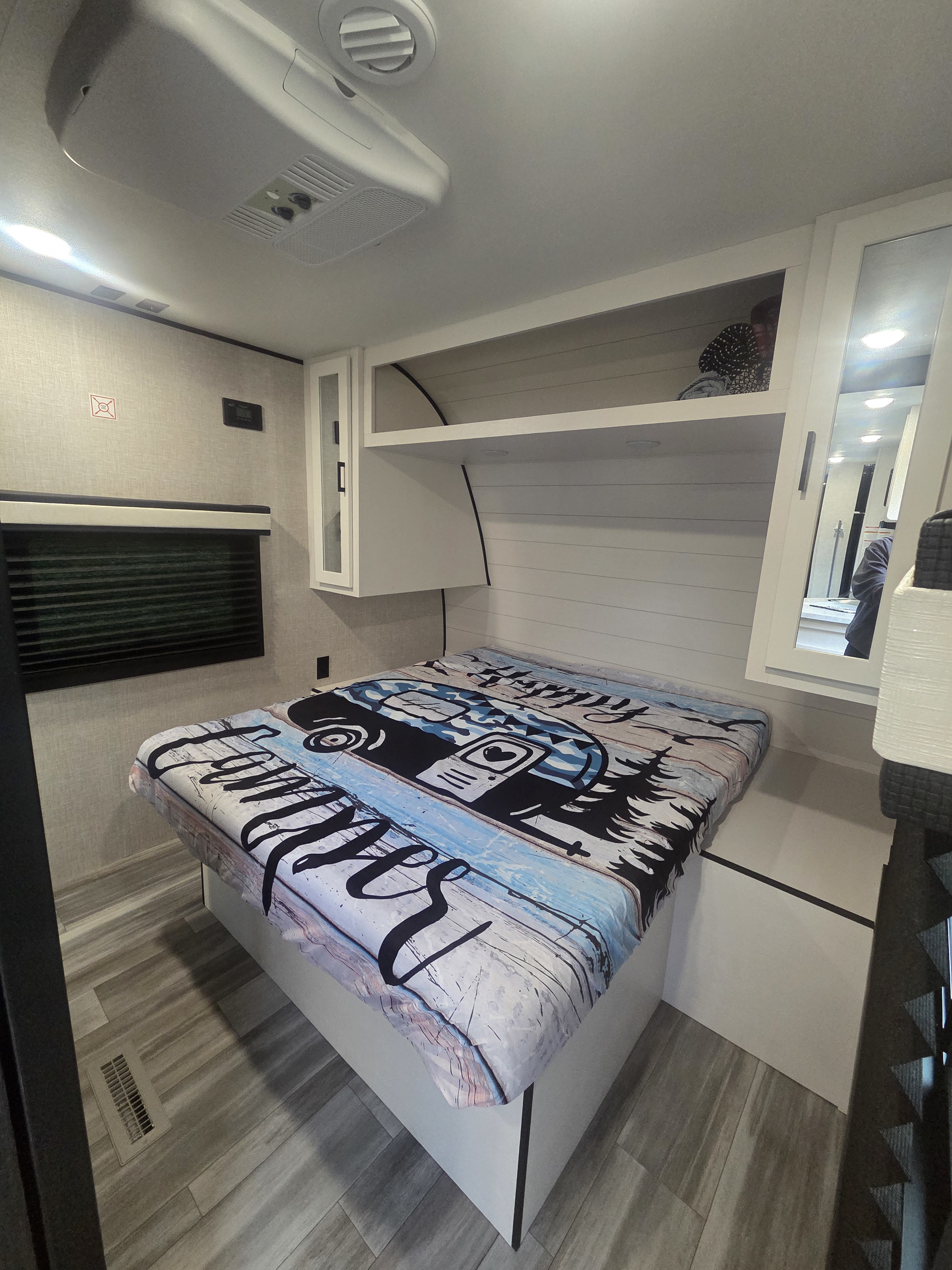 Spacious RV rental bedroom featuring a comfortable bed with a camper graphic blanket, overhead storage, and an AC unit.. Jayco Jay Flight 2024