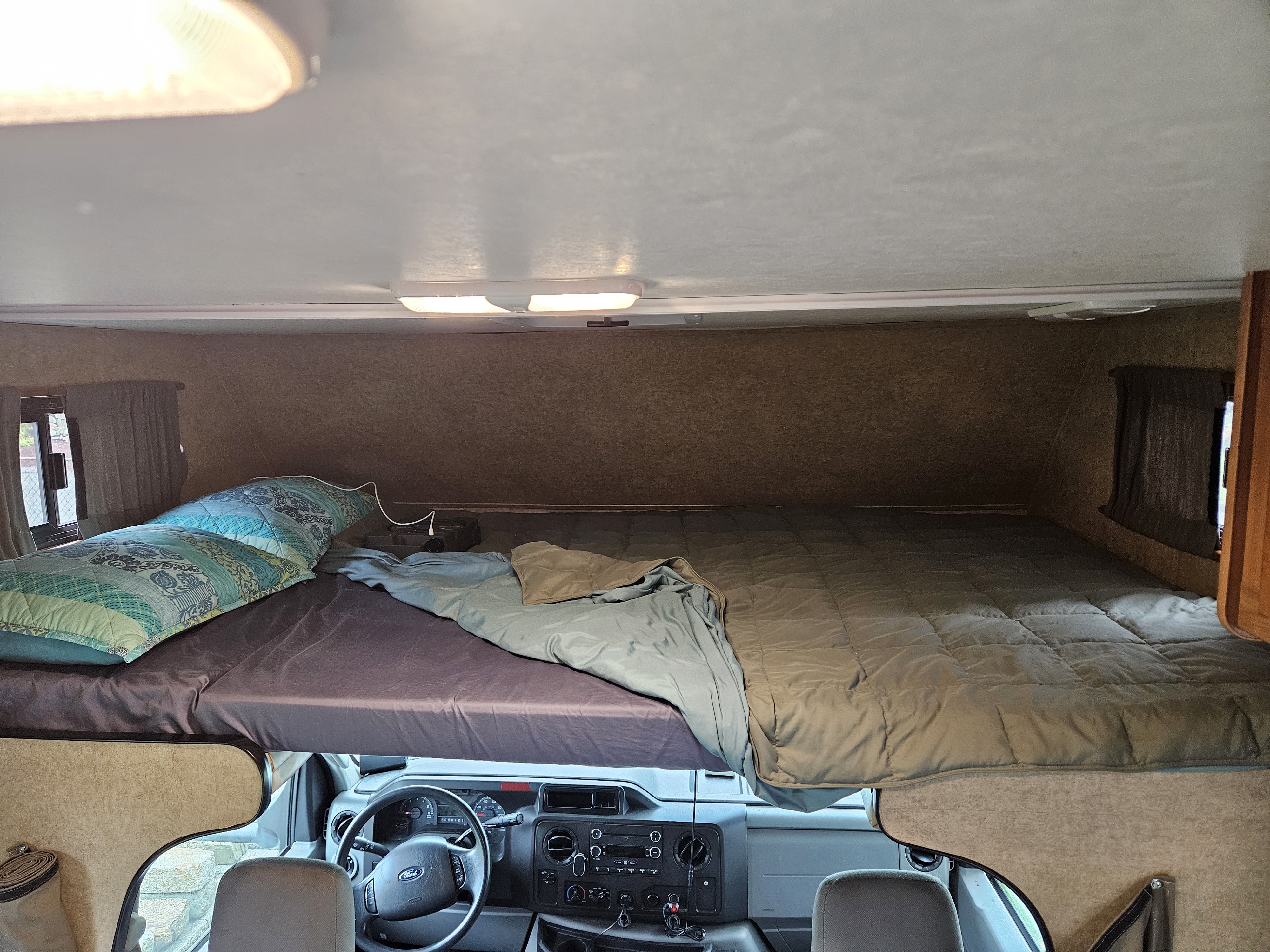 Inside an RV rental: a cozy cab-over bed above the driver's cabin, ready for travel and camping.. Thor Majestic 2018