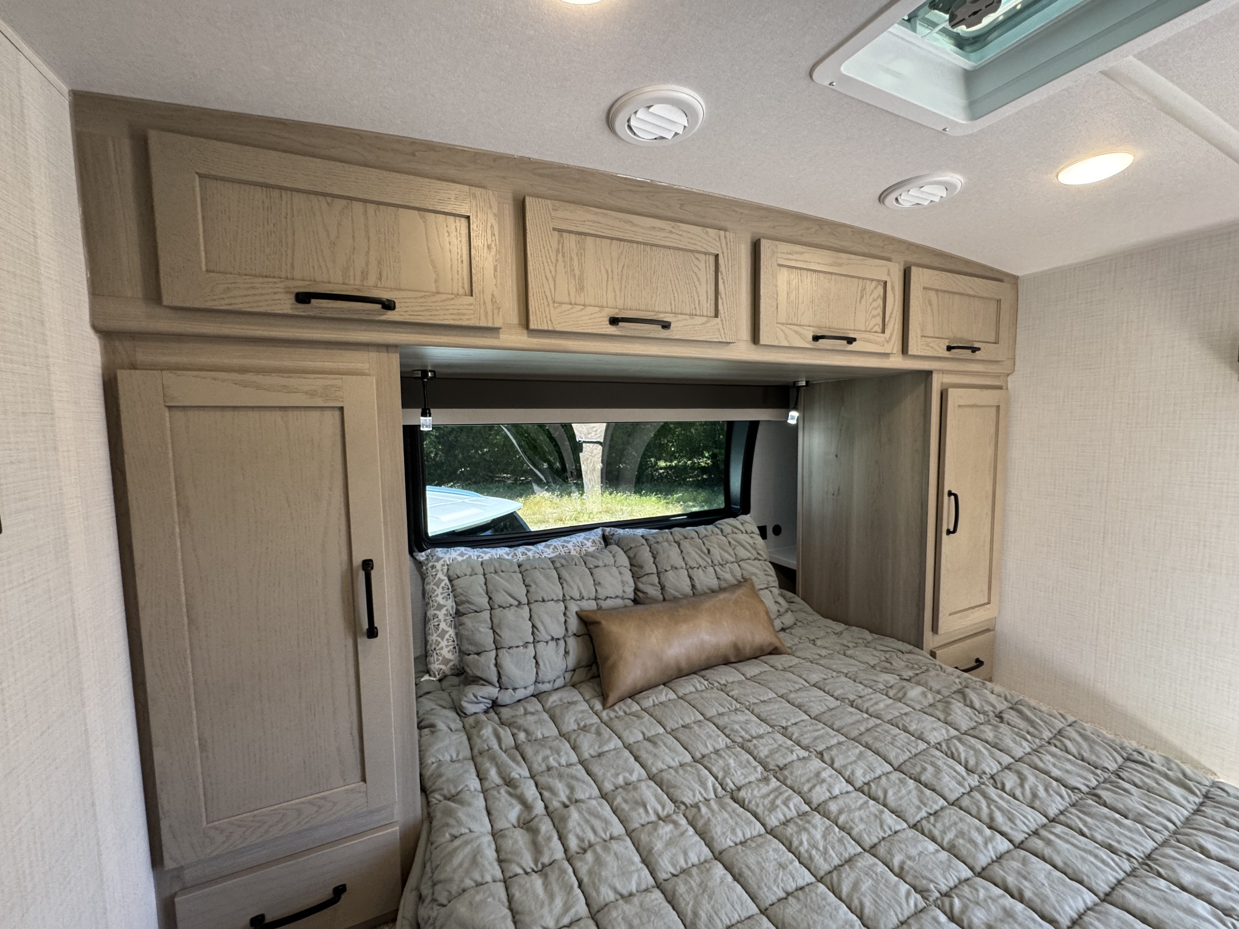 This RV rental's bedroom offers a comfortable bed, ample cabinet storage, and a view of nature. Ideal for travel.. Flagstaff Micro Lite 25DBH 2025