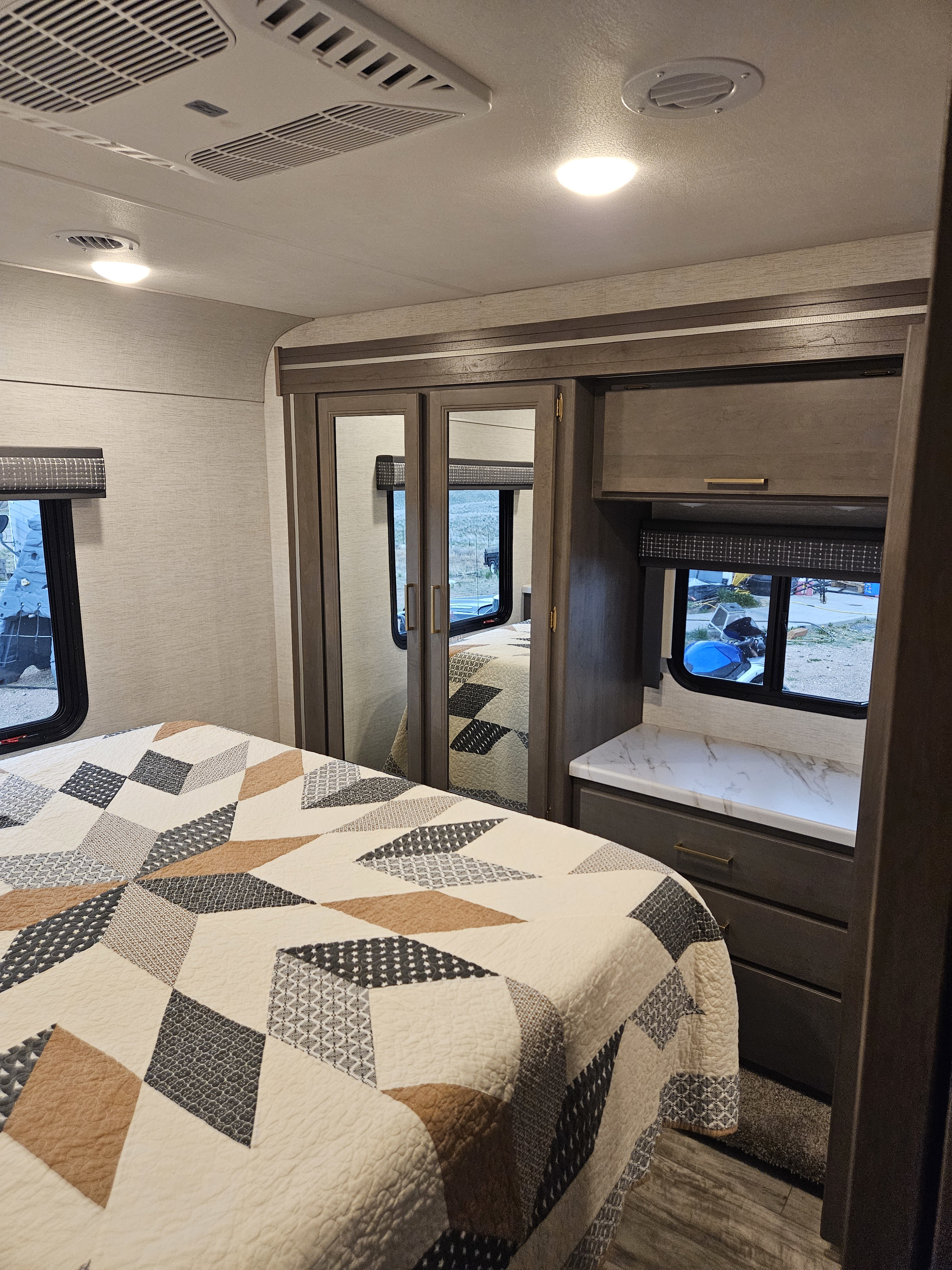 Inside an RV rental: a cozy bedroom features a geometric quilt, mirrored closets, and an integrated dresser with window.. Thor Chateau 2024