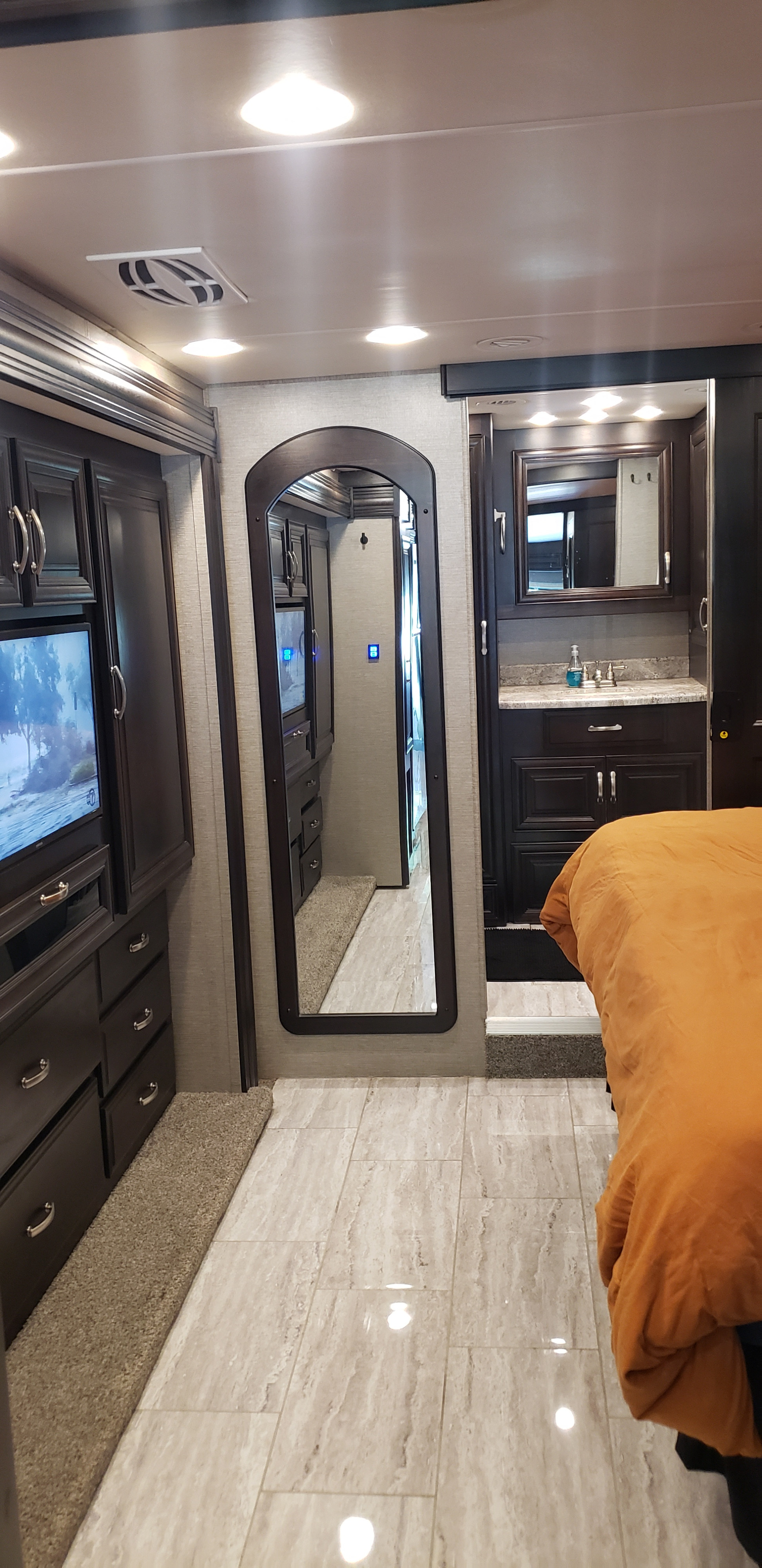 Spacious RV rental interior featuring dark wood cabinets, a TV, full-length mirror, tiled floor, and a modern bathroom vanity.. Berkshire Berkshire Motorhome 2019