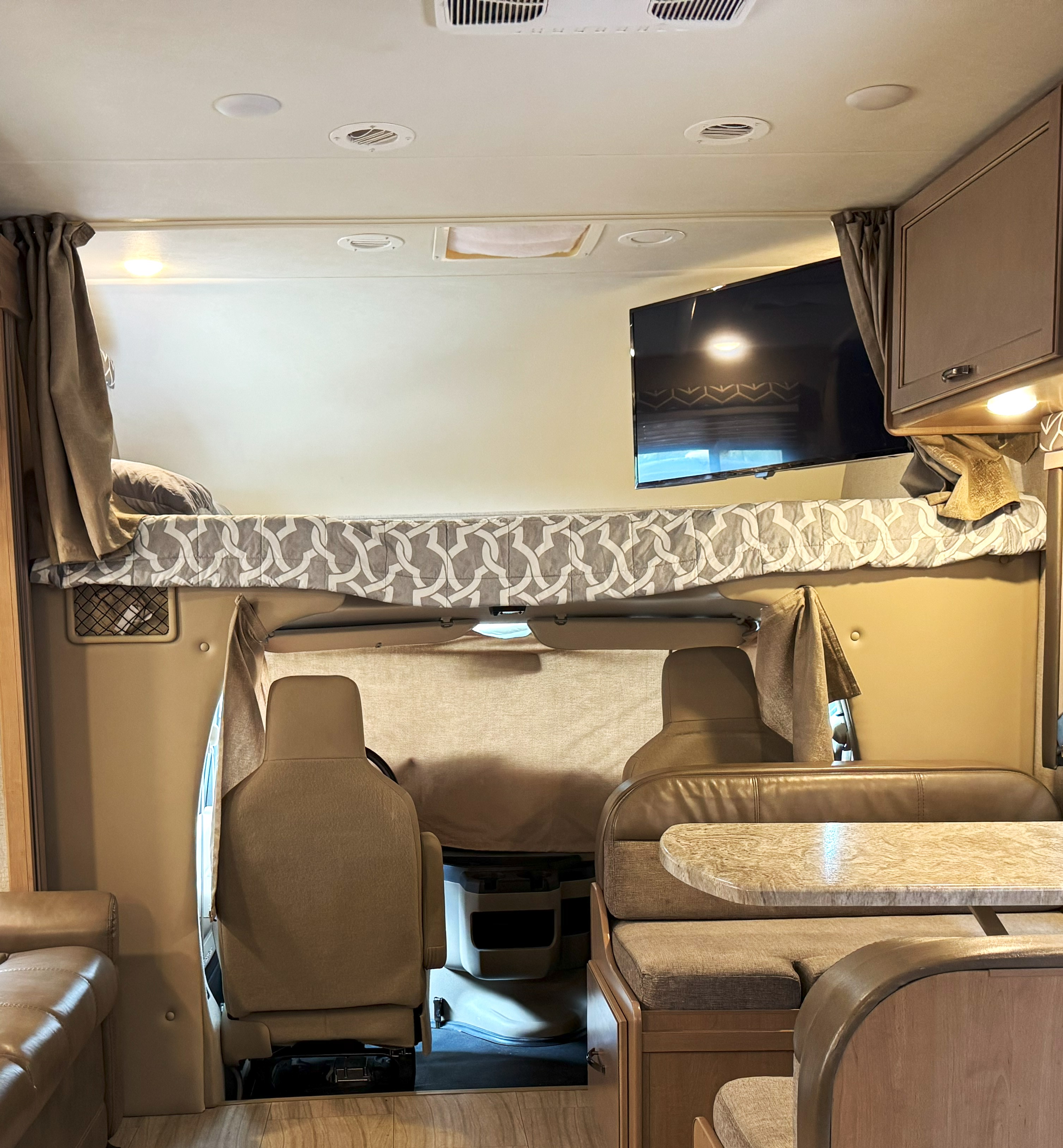 Inside a cozy RV rental: an overhead bunk bed, driver's area, and dinette make for comfortable travel.. Thor Daybreak 2020