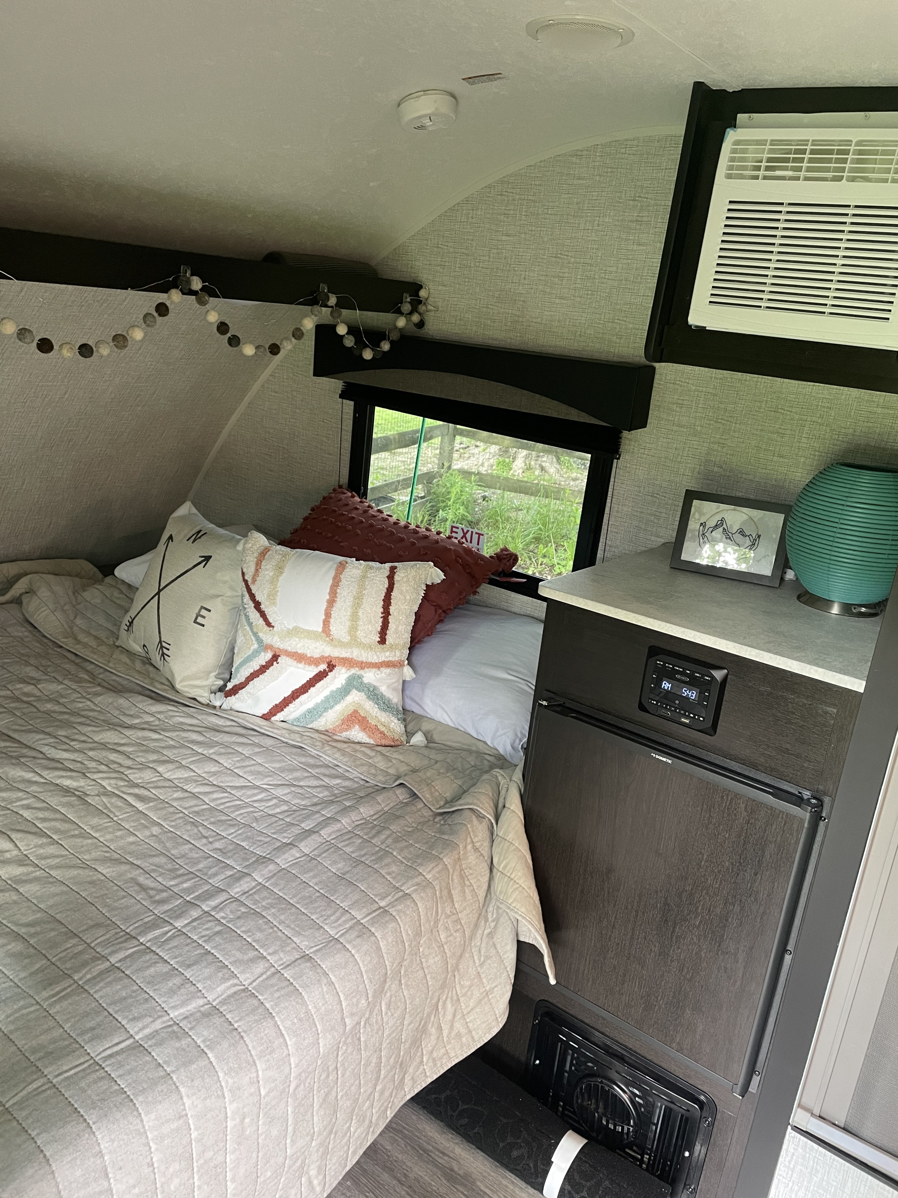 RV rental: Cozy compact sleeping area featuring a comfy bed with decorative pillows, mini-fridge, AC, and window.. Braxton Creek Bushwhacker Plus 2021