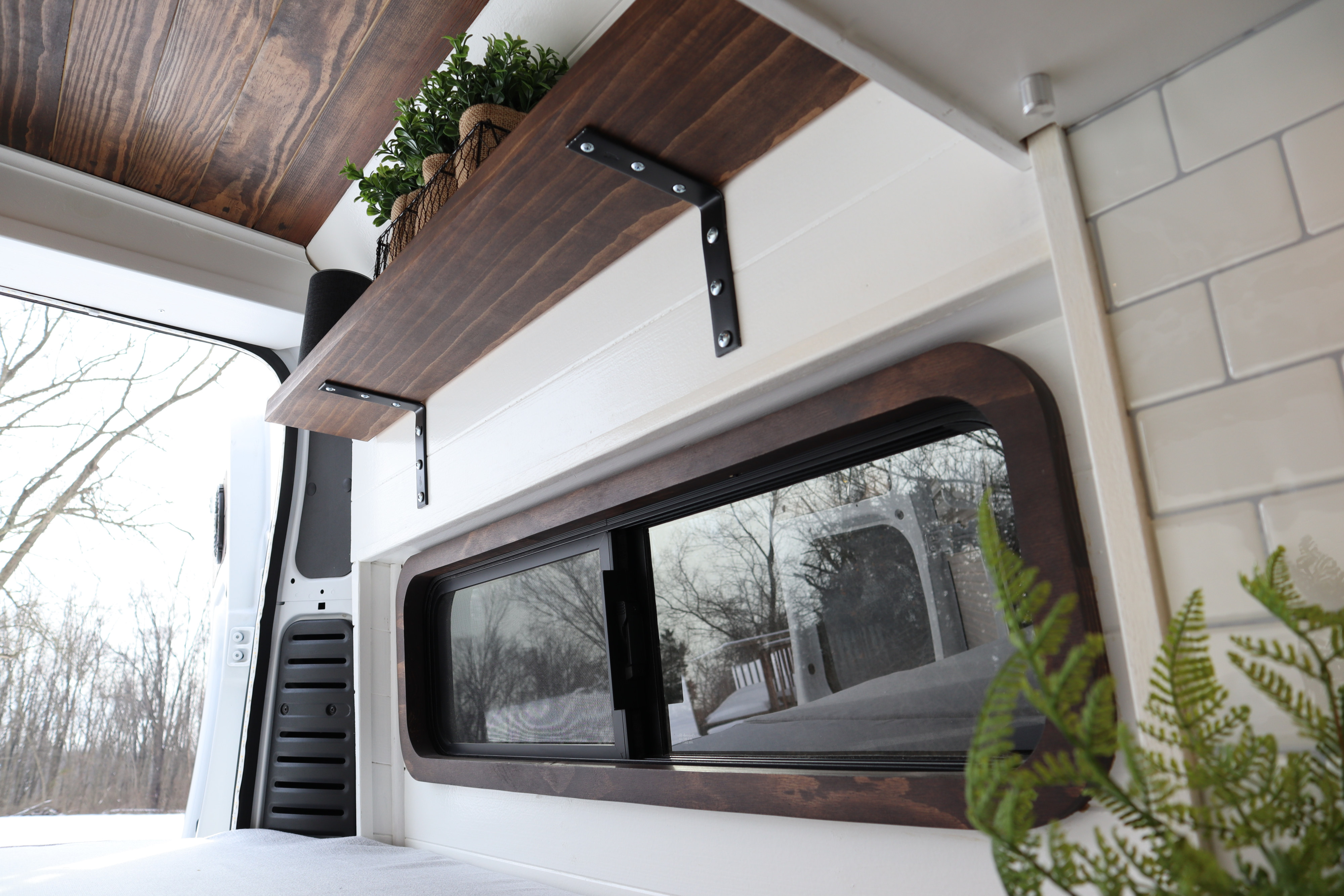 Cozy wood and white camper van rental interior with a custom shelf and snowy window view.. Dodge Ram 1500 2019