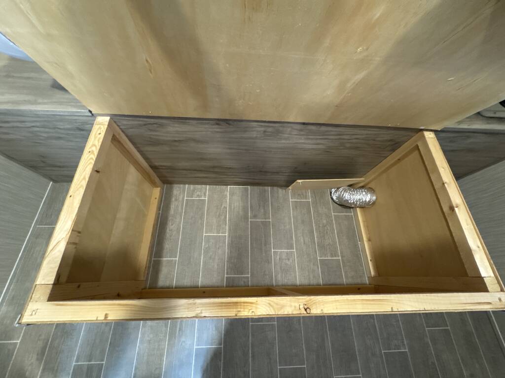 RV rental under-bed storage unit visible, showing wood construction and flexible ductwork on a tile floor.. Forest River Cherokee Alpha Wolf 2020