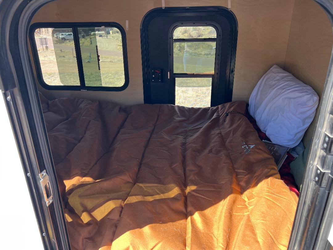 Compact RV rental interior featuring a cozy bed, a white pillow, and two windows for outdoor views.. Outbound Outbound Extreme 2019