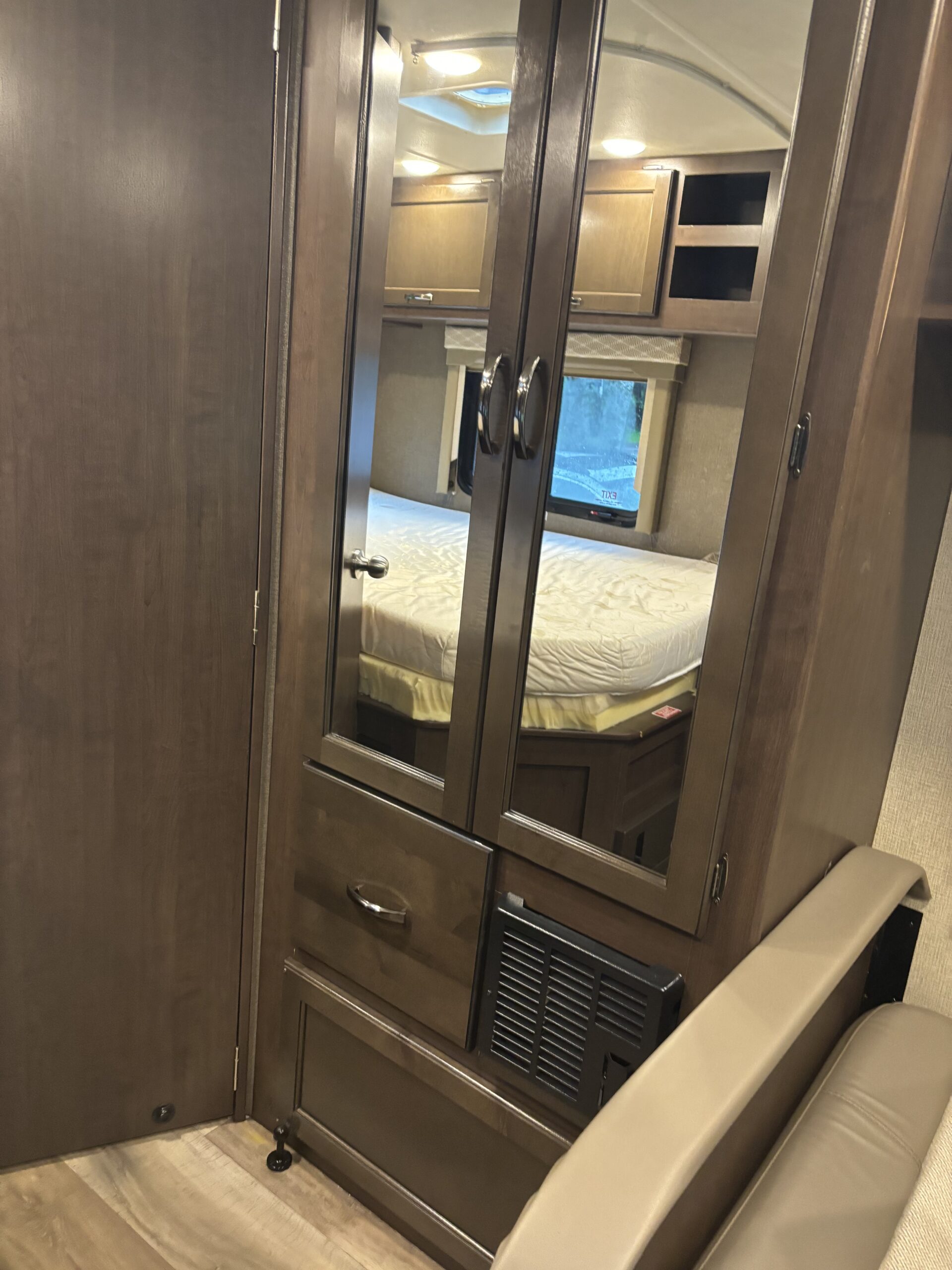 Inside an RV rental, a mirrored wardrobe reflects the cozy bedroom area with bed, window, and overhead cabinets.. Thor Freedom Traveler 2019