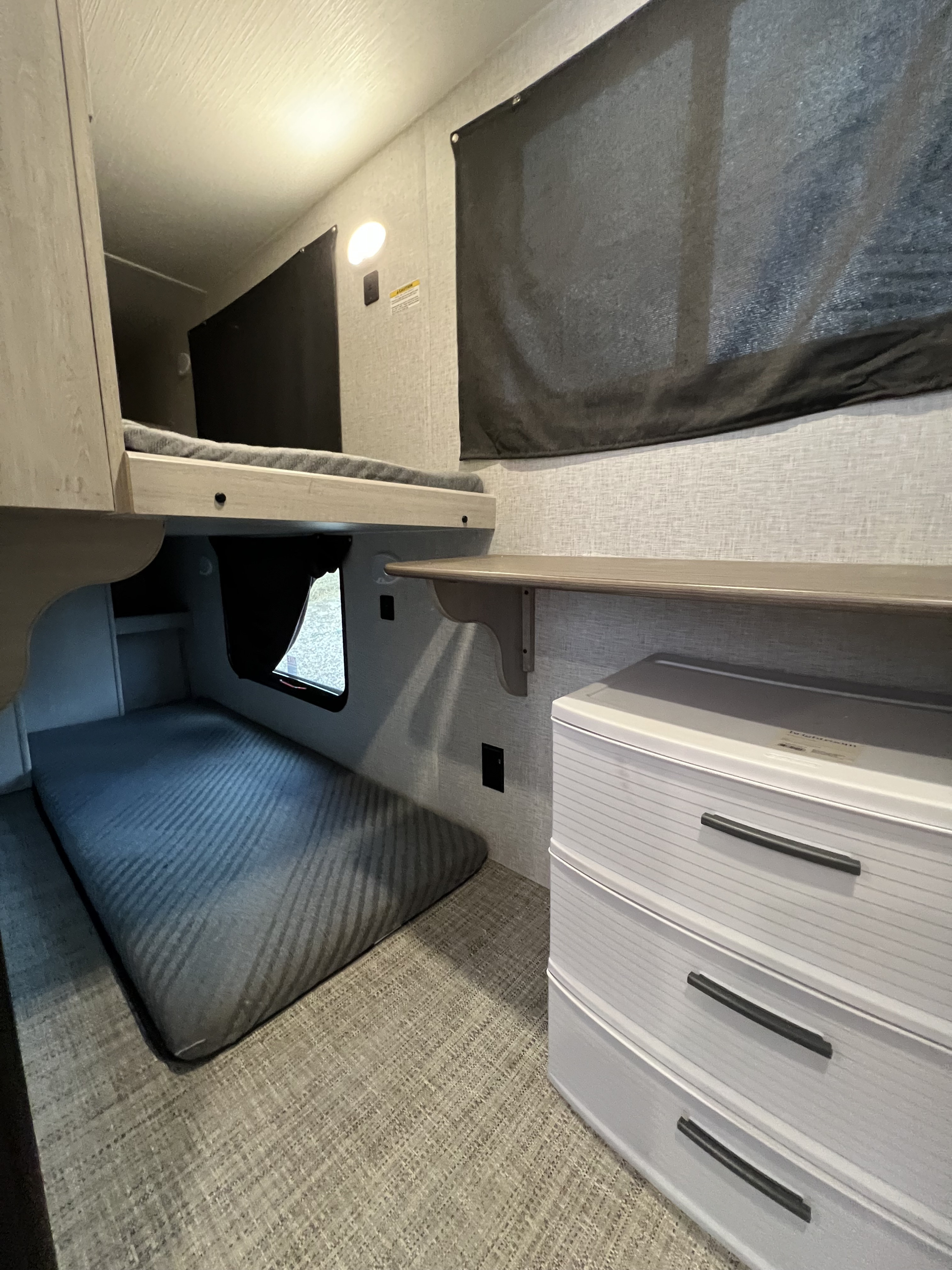RV rental's sleeping area with a lower mattress, upper bunk, a convenient shelf, and practical storage drawers.. Crossroads RV Zinger 2024