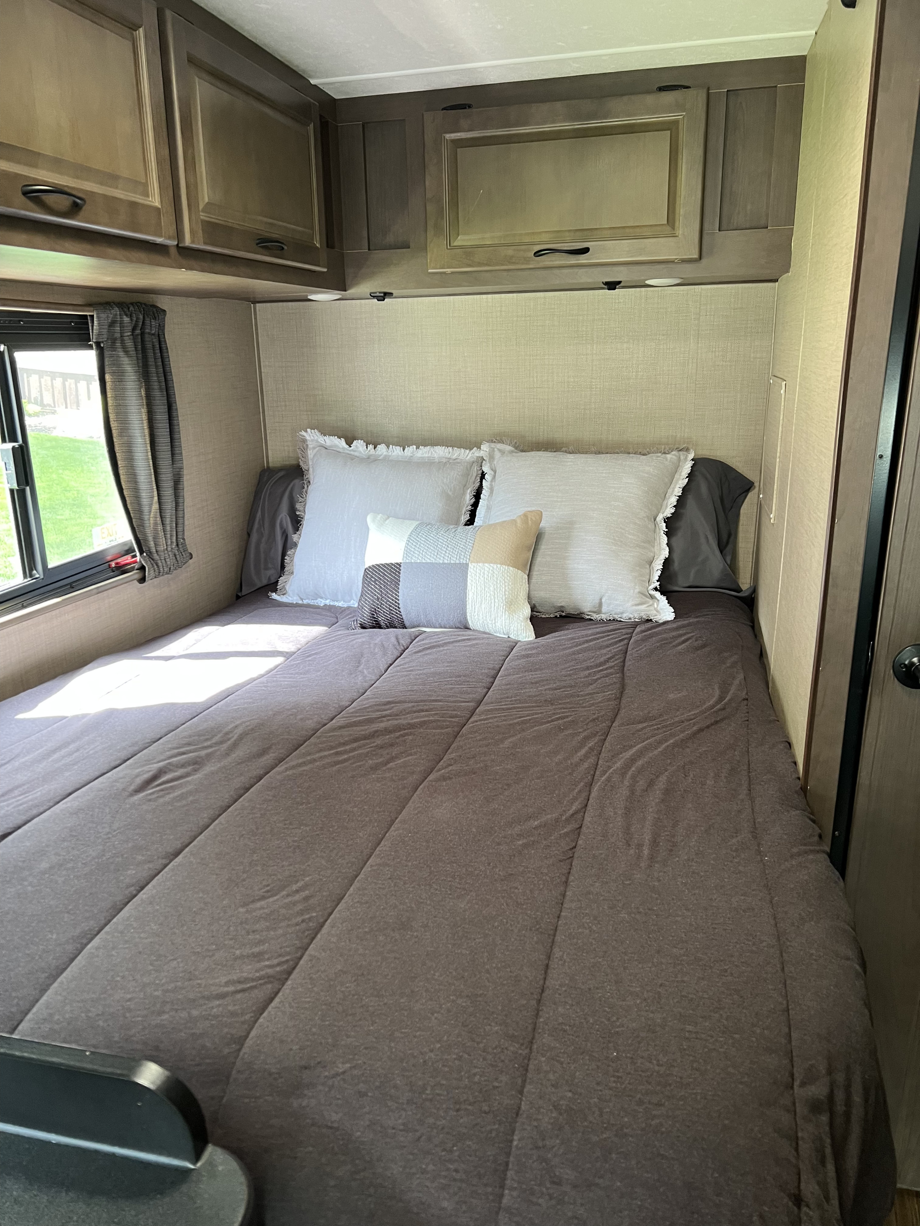 Cozy RV rental bedroom view: a neatly made bed with pillows, practical overhead cabinets, and a window showcasing greenery.. Thor Majestic 2018