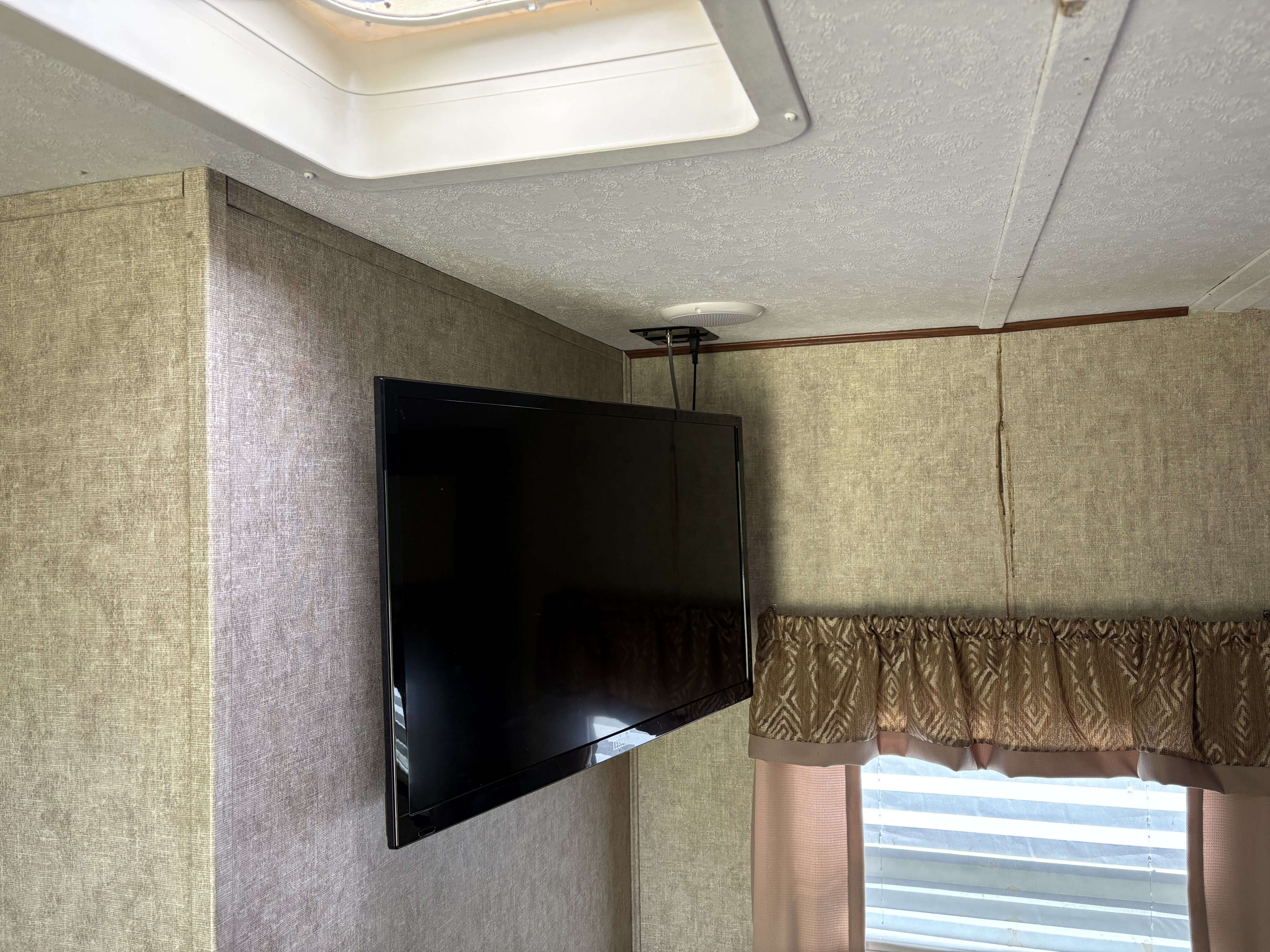Inside an RV rental: a ceiling-mounted TV, skylight, textured walls, and window with valance and blinds for cozy travel.. Tracer Tracer Air 2017