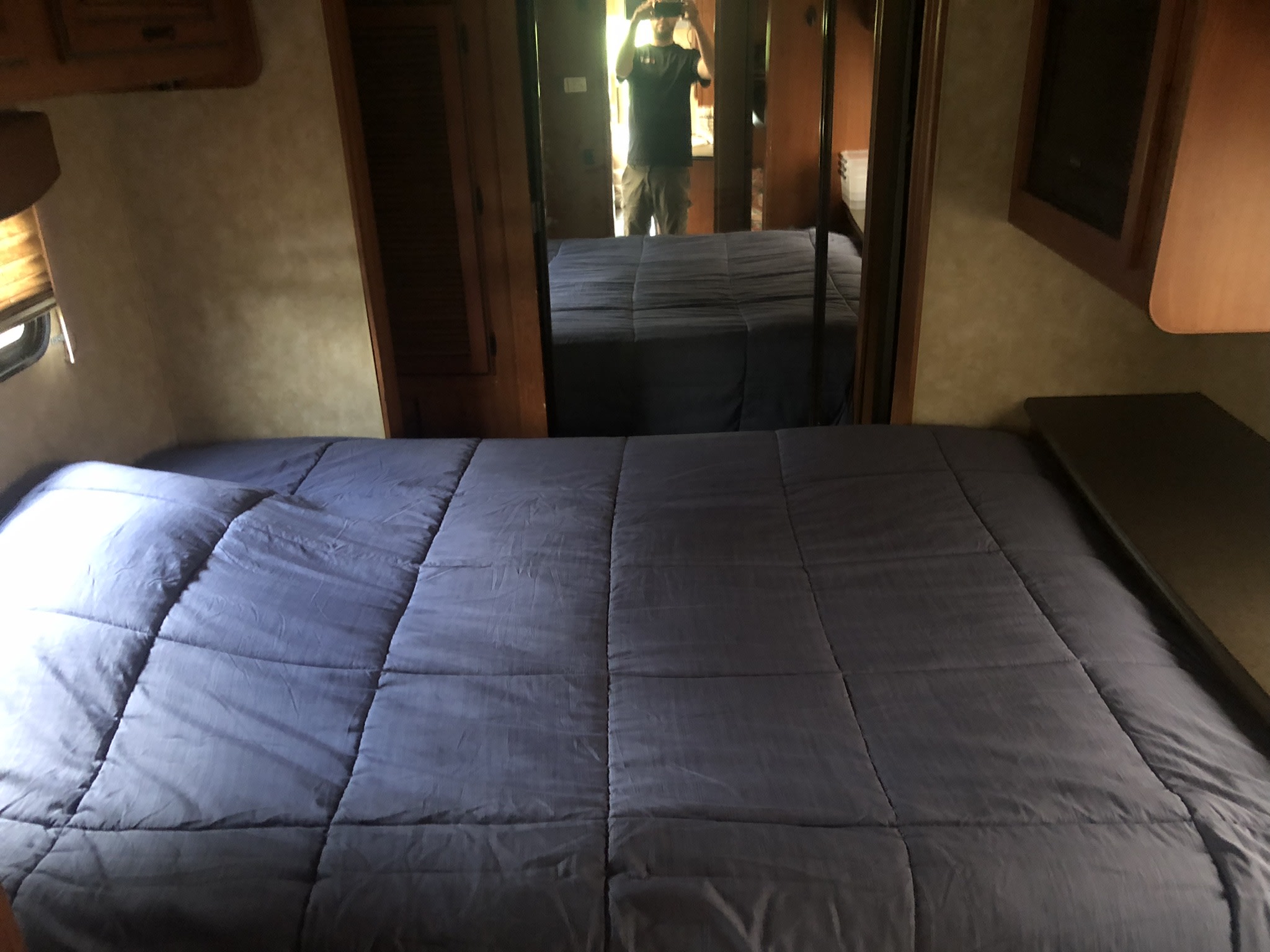 RV rental bedroom with a comfortable bed featuring a blue comforter, built-in cabinetry, and a mirrored wall reflecting the interior.. Forest River Coachmen Cross Country 2011