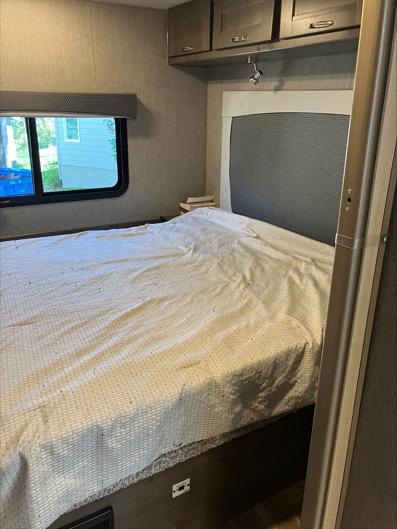 RV rental bedroom interior with a white bed, window, and overhead cabinets. Cozy space for your next trip.. Nexus RV Triumph 2021