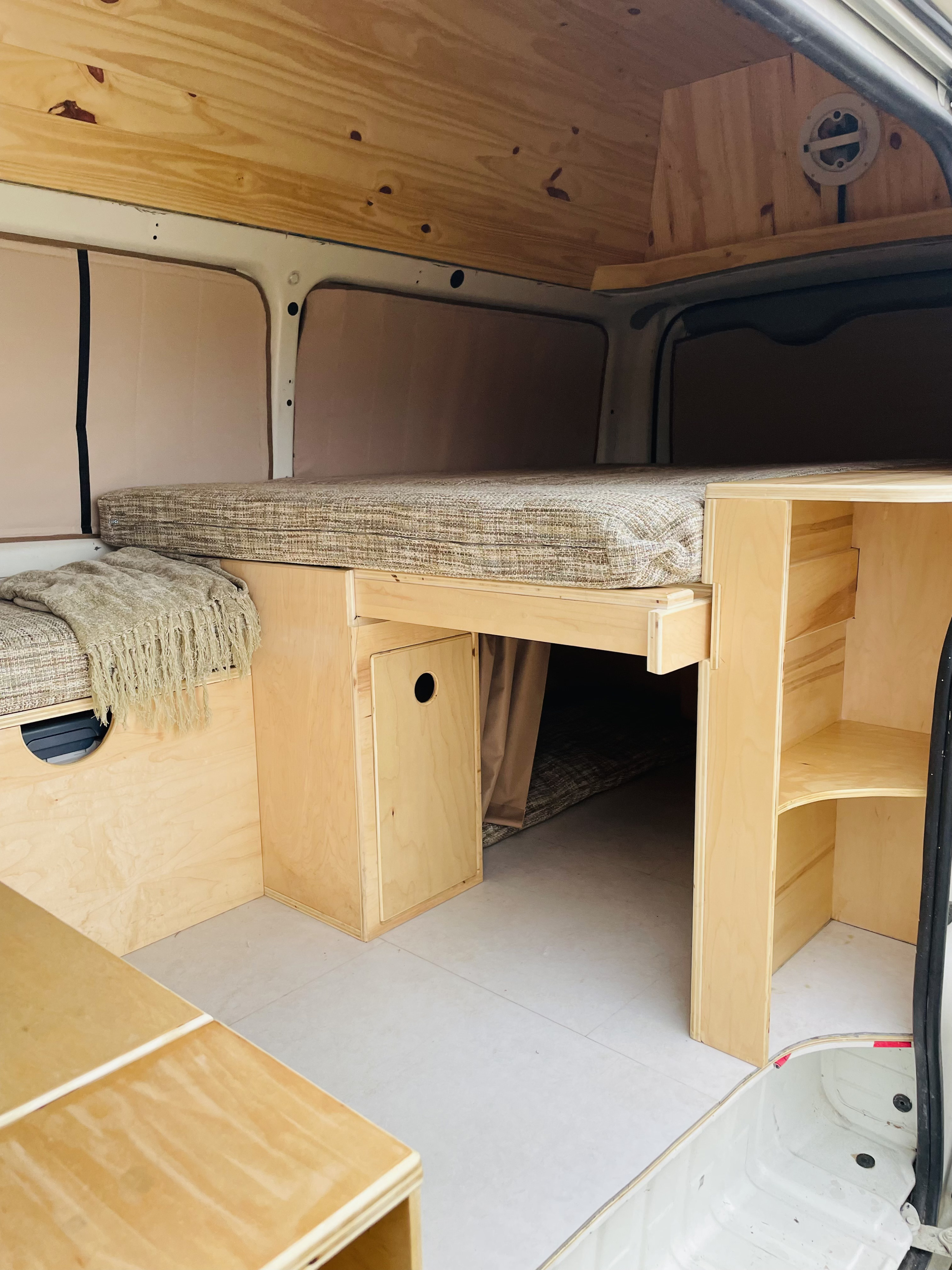 This RV rental interior features a custom wood build, a comfortable bed, smart storage, and window insulation for travel.. Toyota HiAce 2005