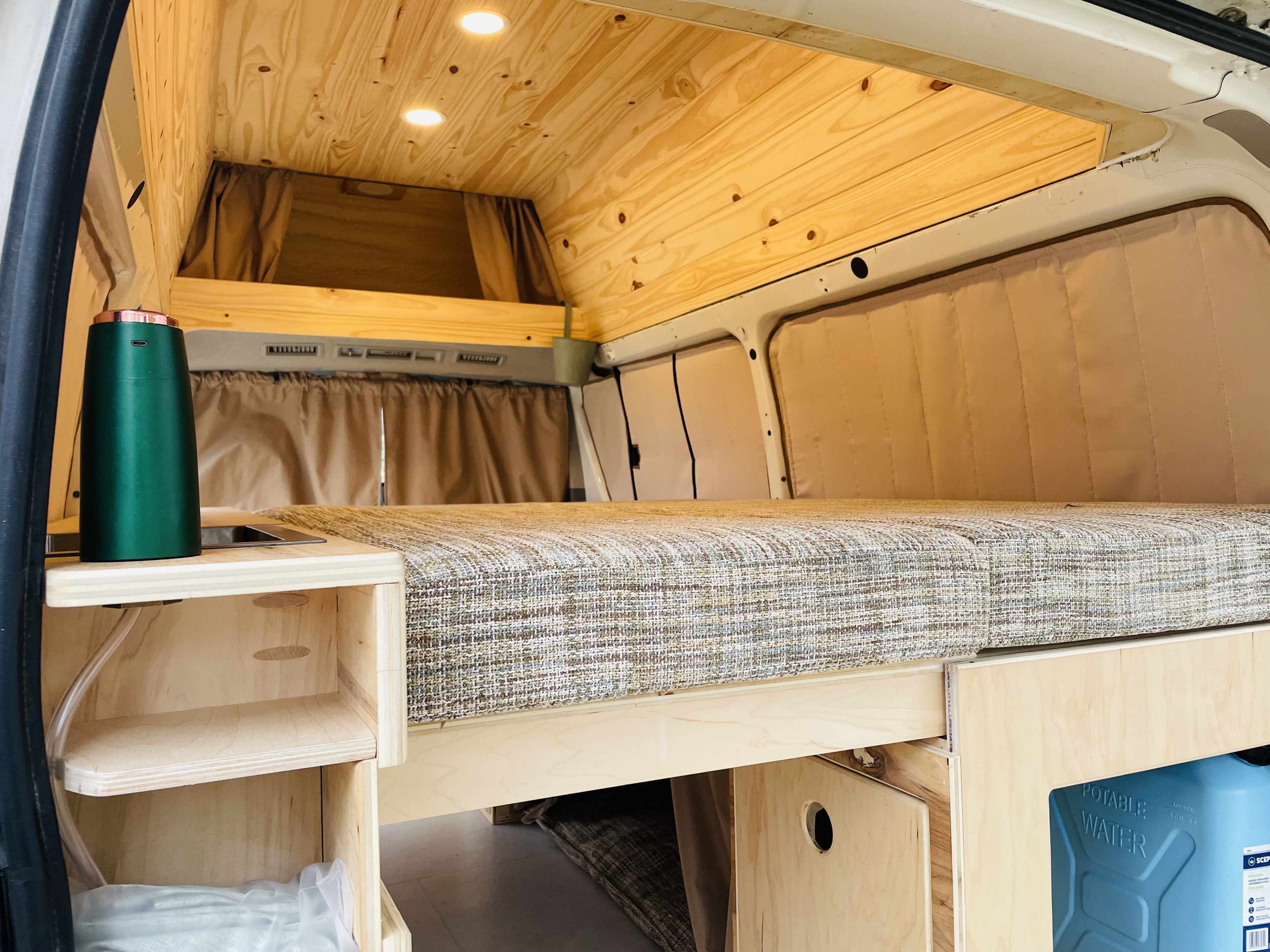 Discover the cozy interior of this RV rental, featuring a comfortable bed, warm wood ceiling, and smart built-in storage.. Toyota HiAce 2005