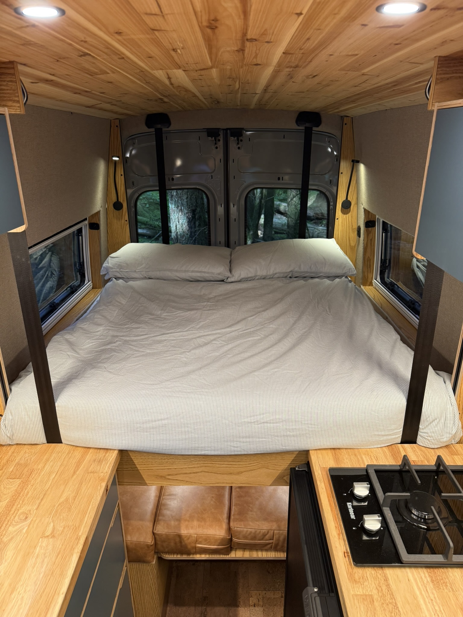 Cozy rv rental: full bed with striped bedding, wooden ceiling, kitchen, seating, and nature views.. Ford Transit 2023
