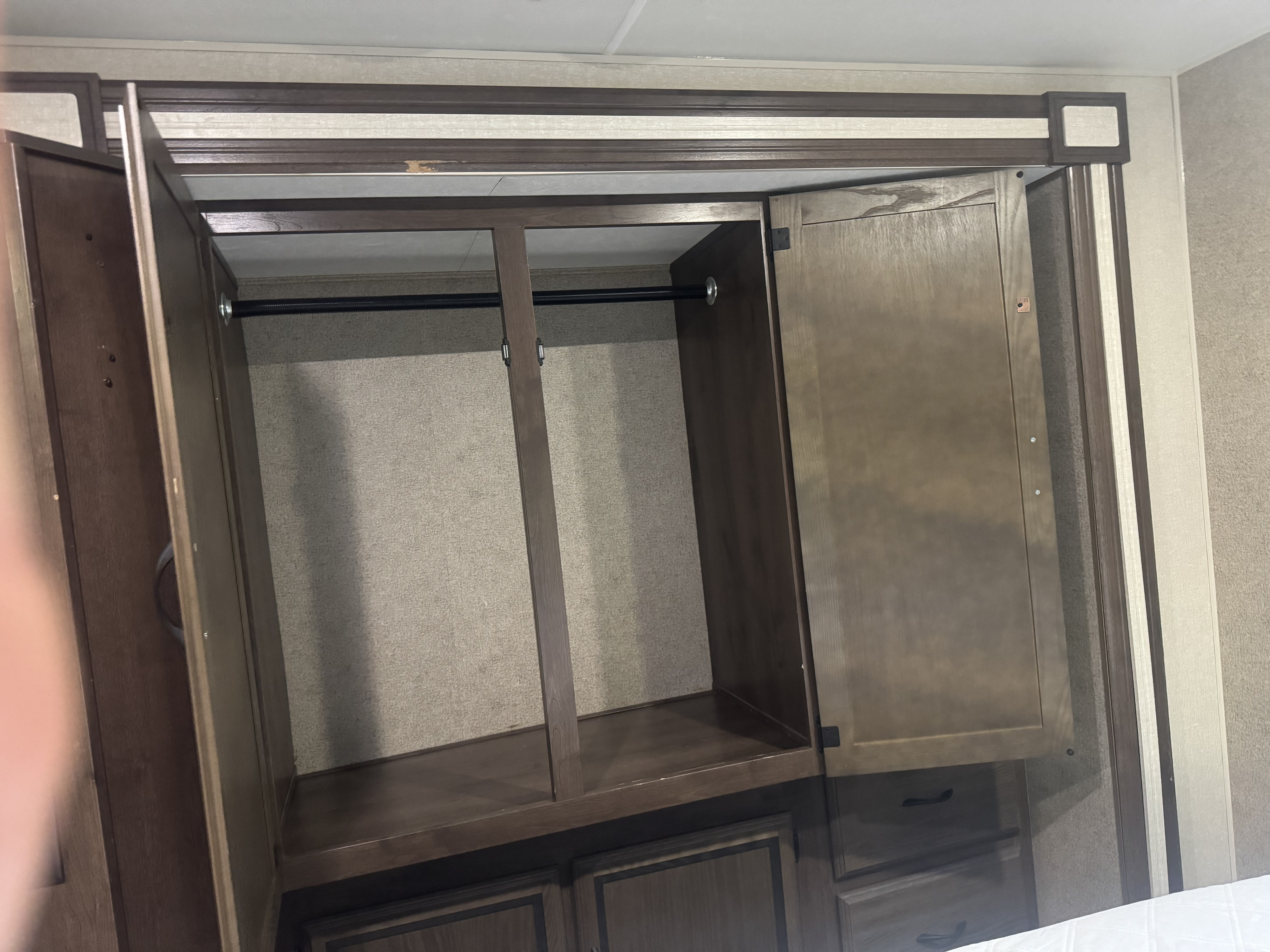 RV rental wardrobe: Open closet with a hanging rod, central divider, and lower storage drawers inside an RV.. Ford Coachman 2018