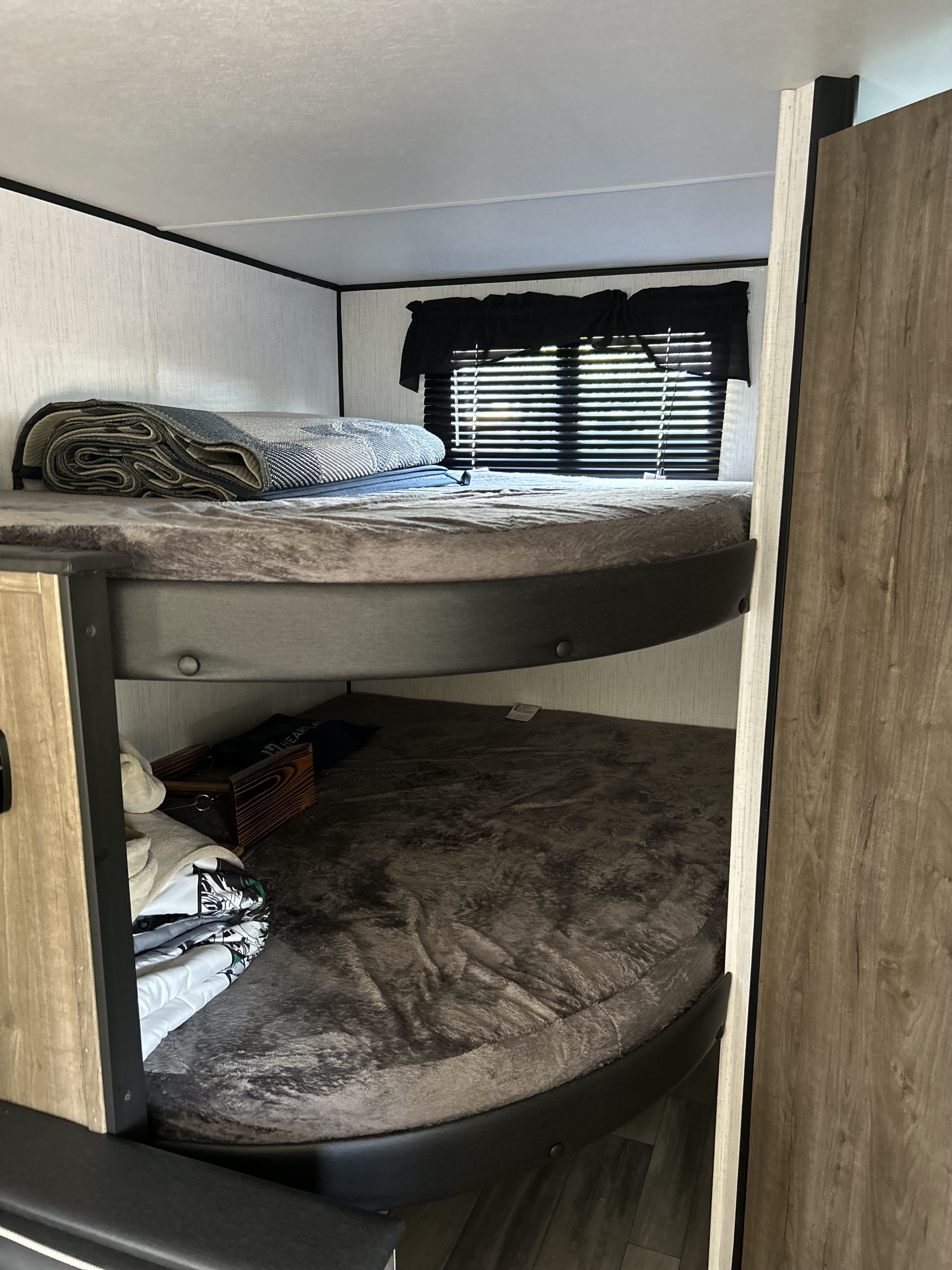 Cozy bunk beds inside an RV rental, featuring soft bedding, a rolled blanket on top, and a window with blinds.. Heartland RVs Pioneer 2022