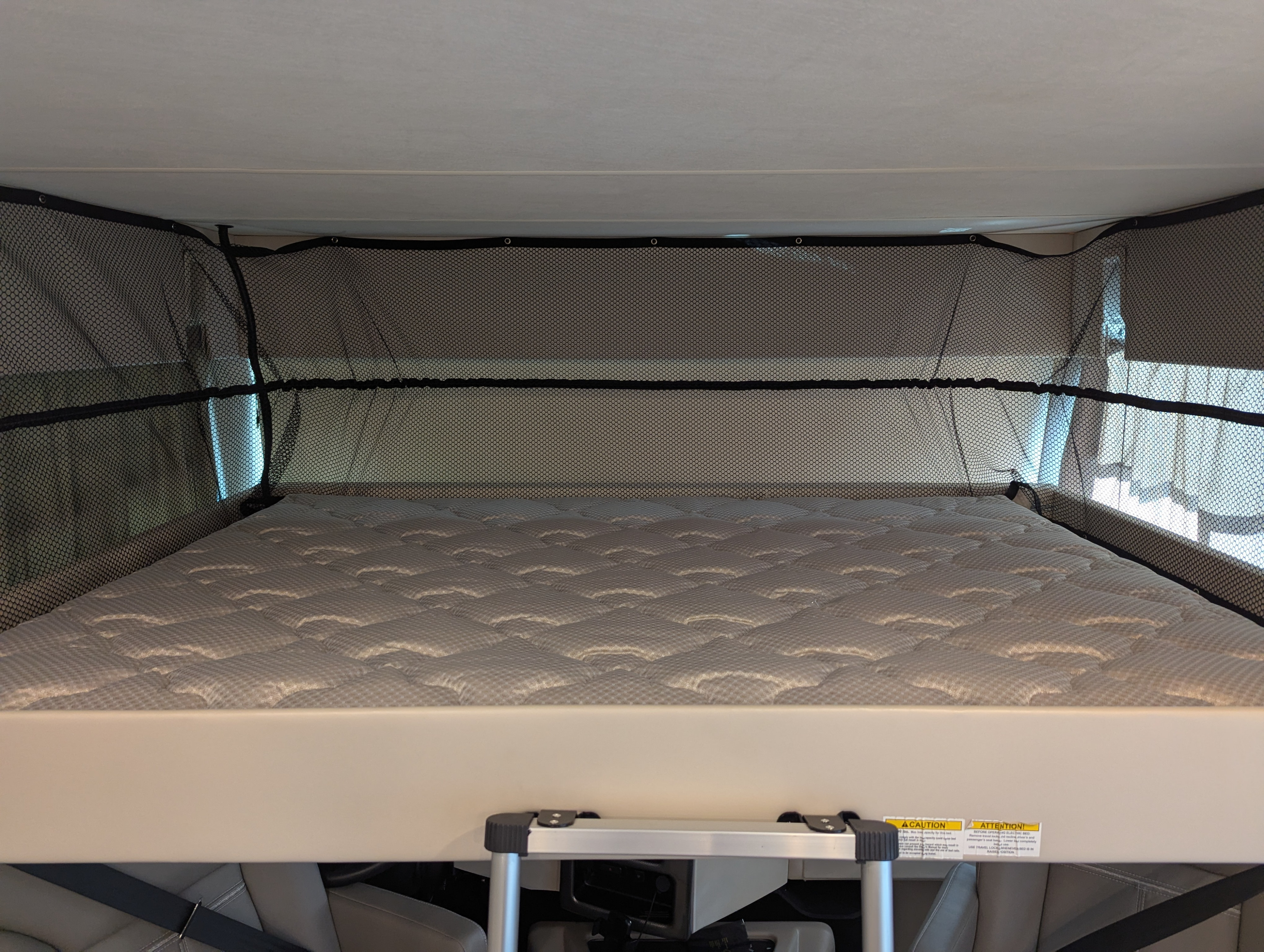 RV rental: Bright view of an overhead bunk bed with a quilted mattress and safety net inside a camper.. Thor Resonate 2025