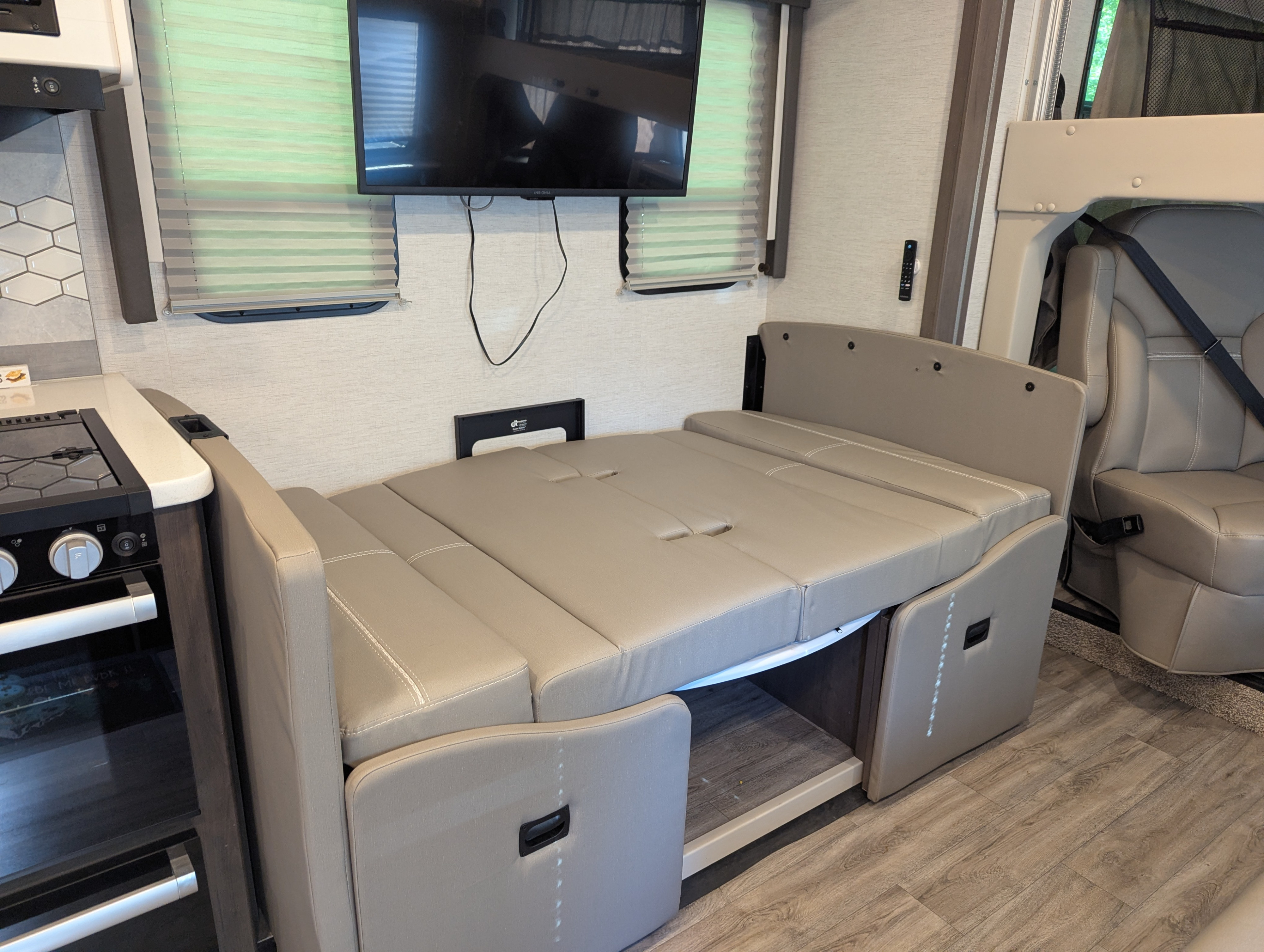 Modern RV rental interior: convertible dinette/bed, kitchen, wall-mounted TV, and plush front seating.. Thor Resonate 2025