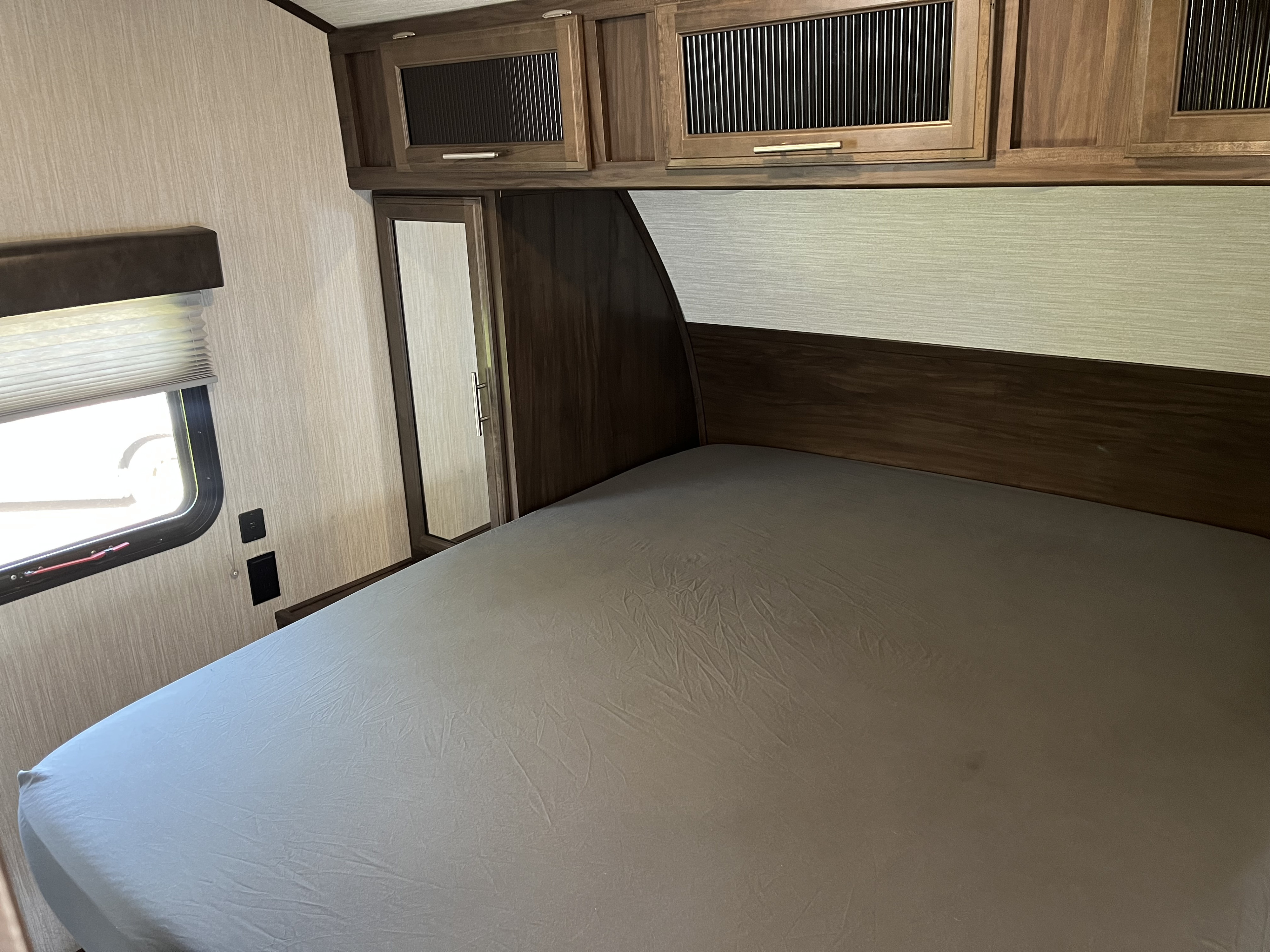 RV rental bedroom: light gray bed, dark wood accents, overhead storage, mirrored closet, and window with outlets.. Forest River Cherokee Alpha Wolf 2020