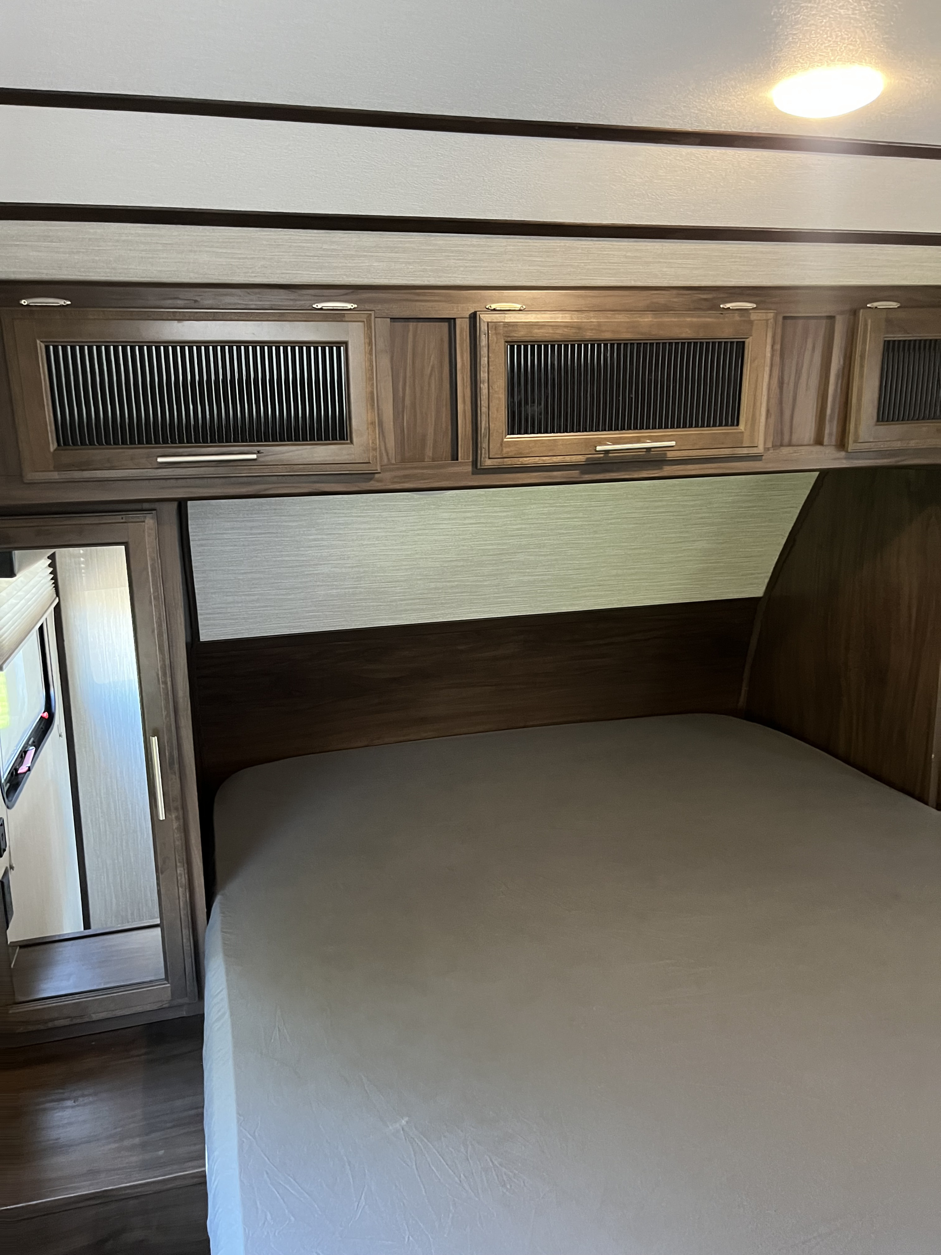 Interior view of an RV bedroom featuring a bed, overhead cabinets, and a light. Perfect for your next rv rental adventure.. Forest River Cherokee Alpha Wolf 2020