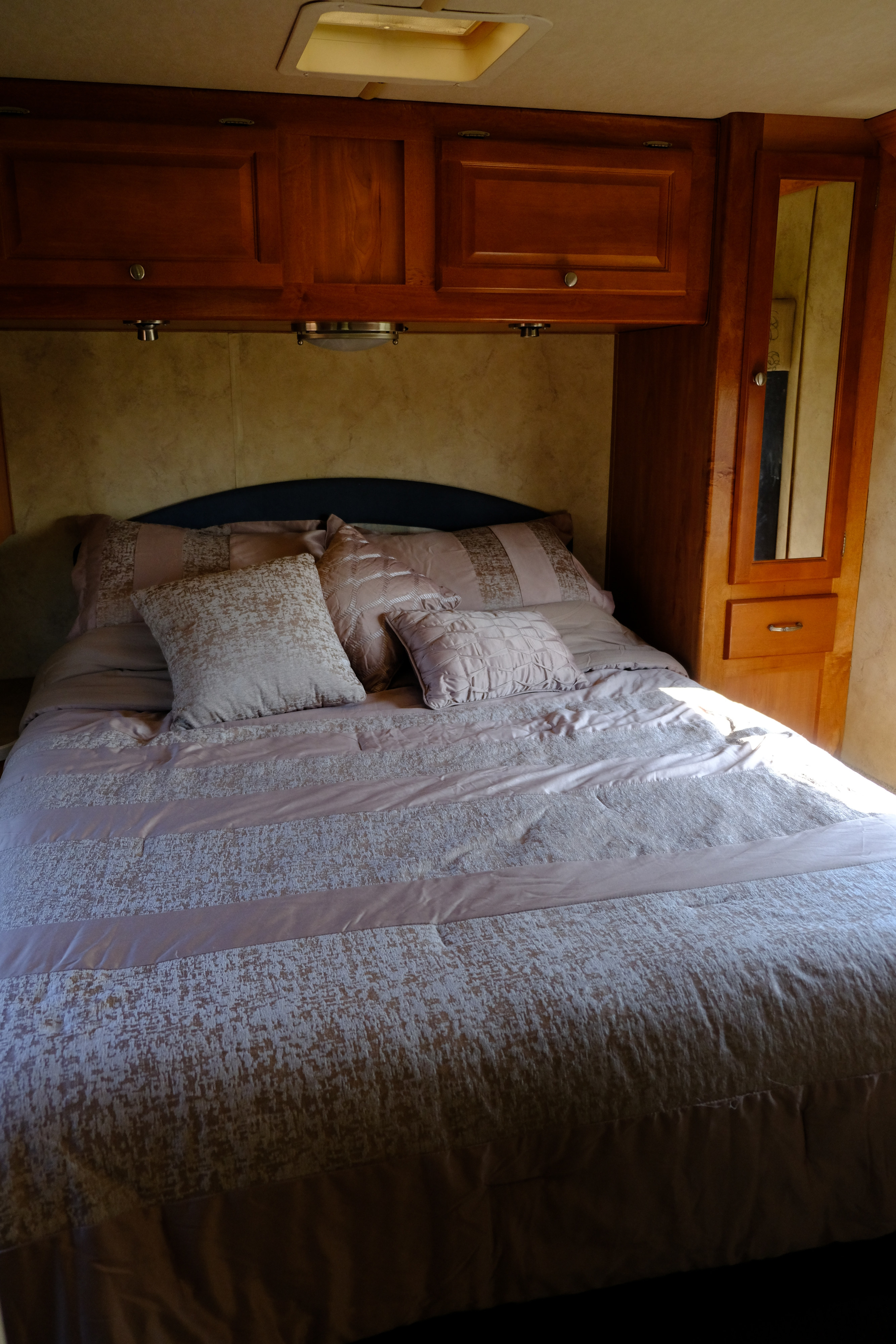 Serene RV rental bedroom: cozy bed with plush pillows, wooden overhead cabinets, and mirrored wardrobe for a relaxing stay.. Gulf Stream Independence 2006