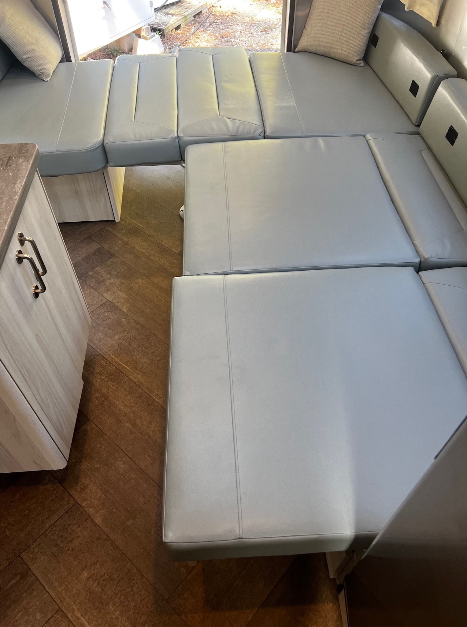 Light grey RV rental interior with convertible seating for sleeping. Features wood-look herringbone floor and built-in cabinet.. Airstream International 2025