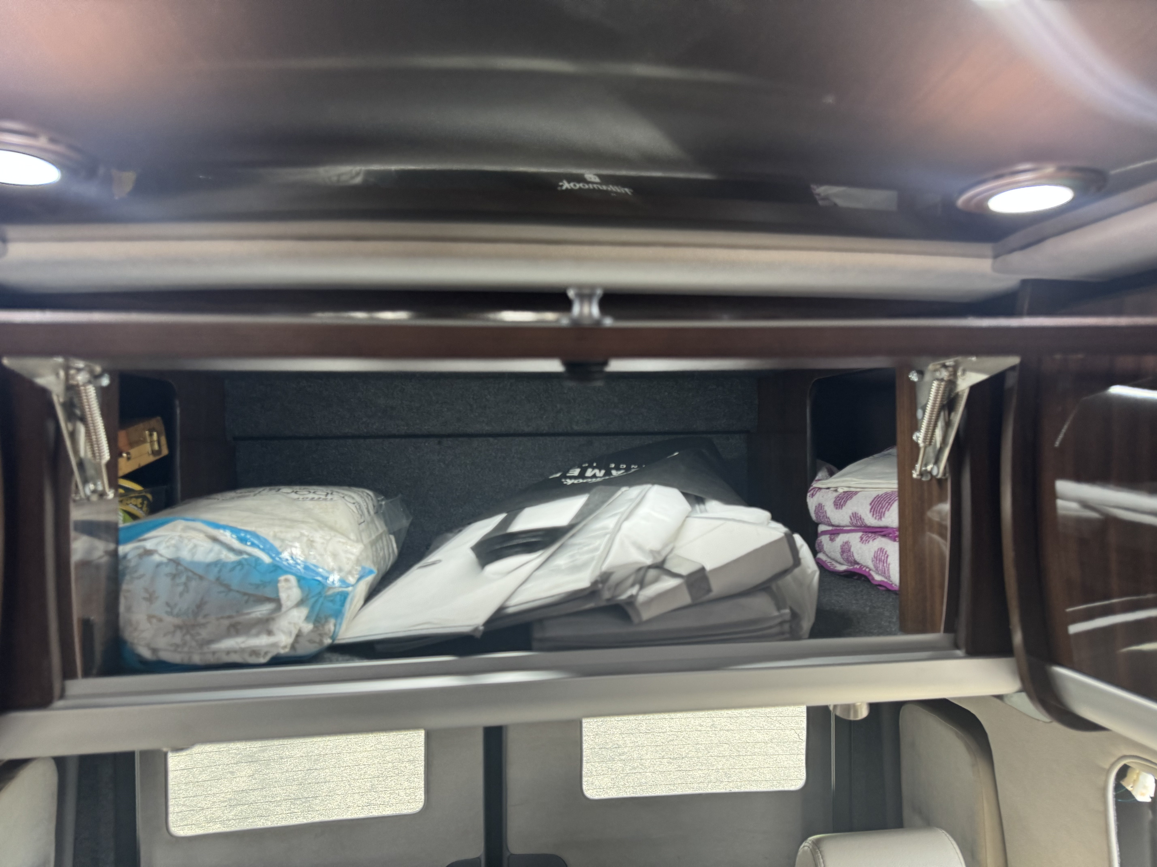 Inside an RV rental's overhead storage: neatly stacked bedding, bags, and folded towels, with visible spring hinges.. Airstream Interstate 2017