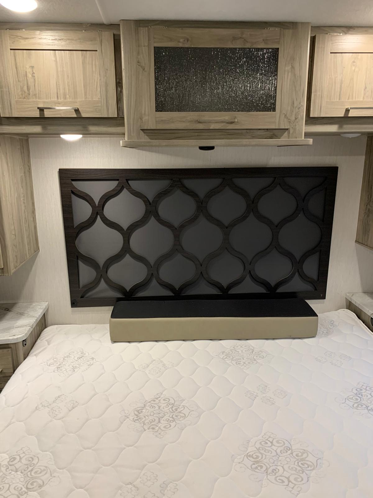 Compact RV rental bedroom featuring a decorative headboard, white mattress, and light wood overhead cabinets.. Forest River Coachmen Pursuit 2022