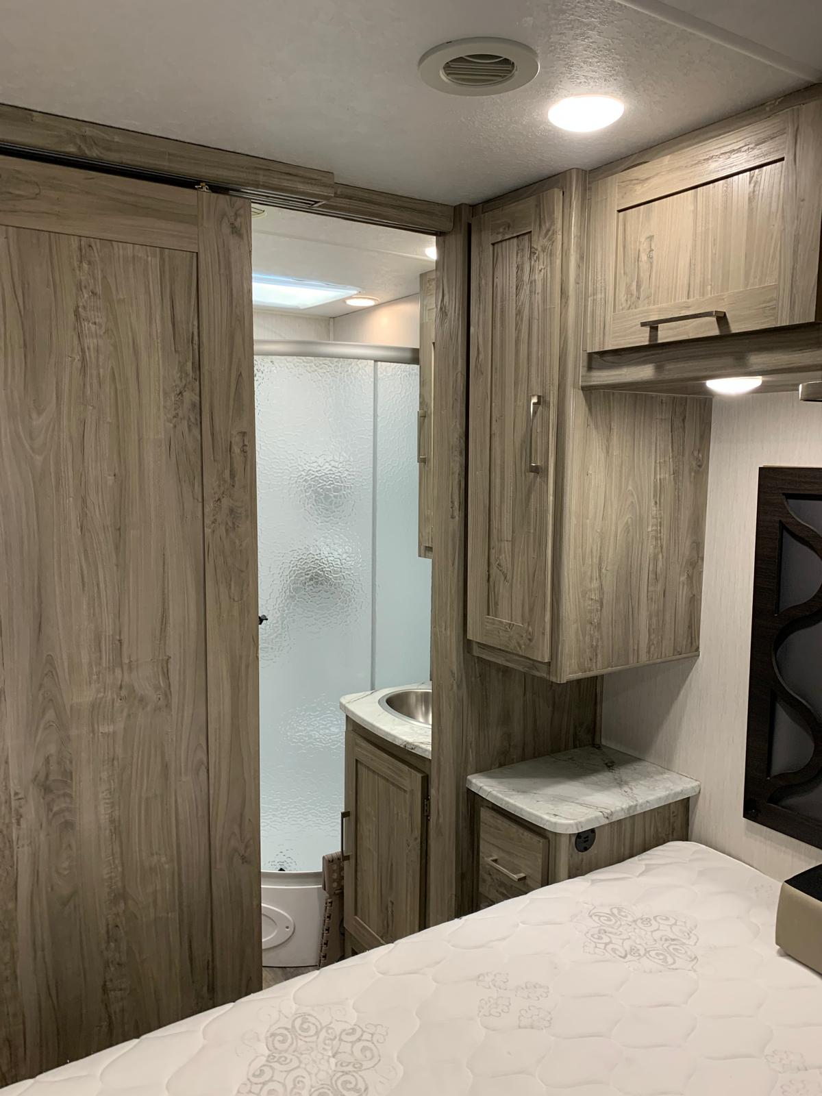 RV rental interior: bedroom with mattress, sliding door to bathroom with shower and sink, built-in light wood cabinetry.. Forest River Coachmen Pursuit 2022