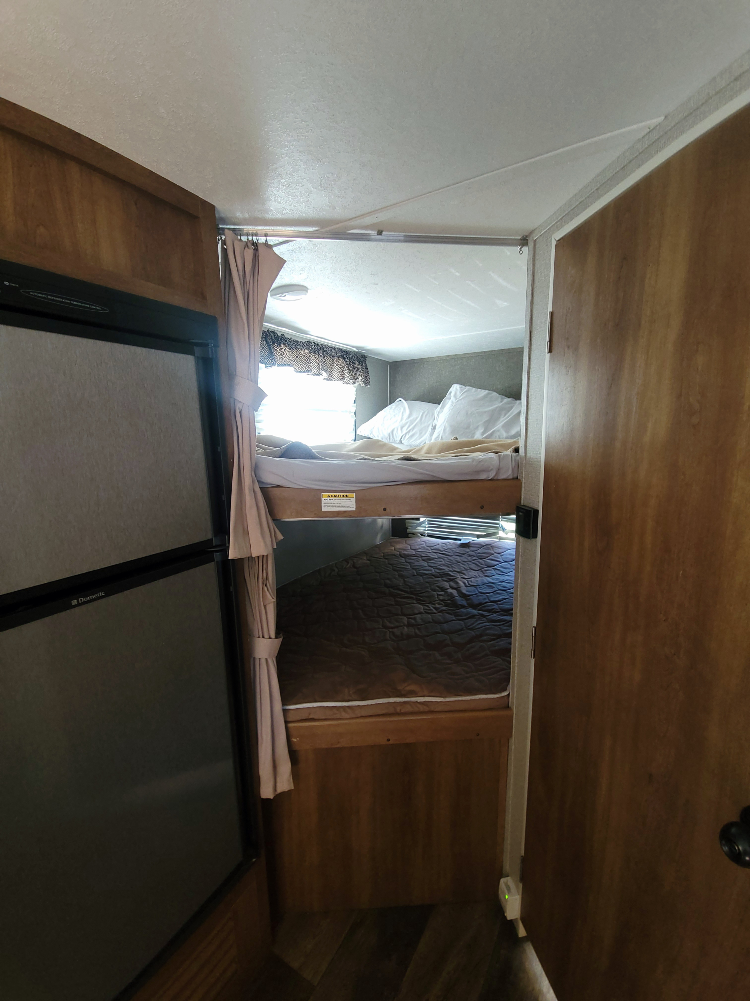 Interior of an RV rental featuring a Dometic refrigerator and cozy bunk beds with privacy curtains.. Keystone RV Springdale 2017