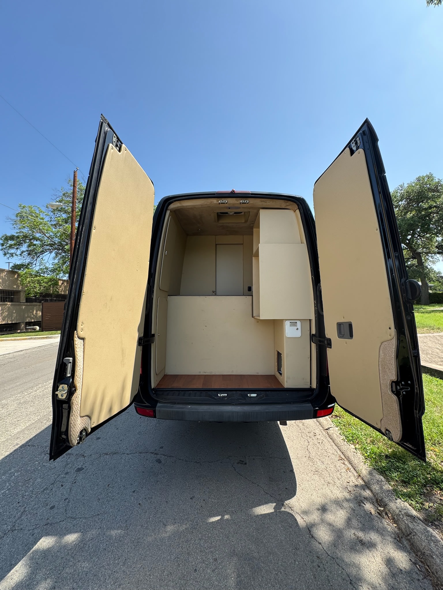 Rear view of a custom-built RV rental van with open doors, revealing a beige interior conversion and wood floor.. Mercedes-Benz Sprinter 2015
