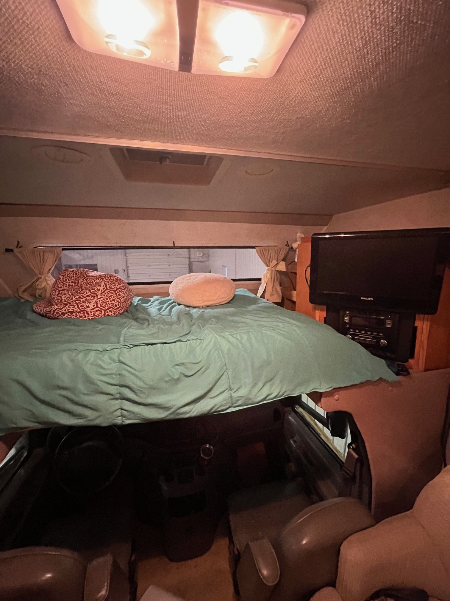 This RV rental interior features a cozy cab-over bunk bed with teal bedding, pillows, a TV, and windows.. Gulf Stream Ultra Supreme 2002