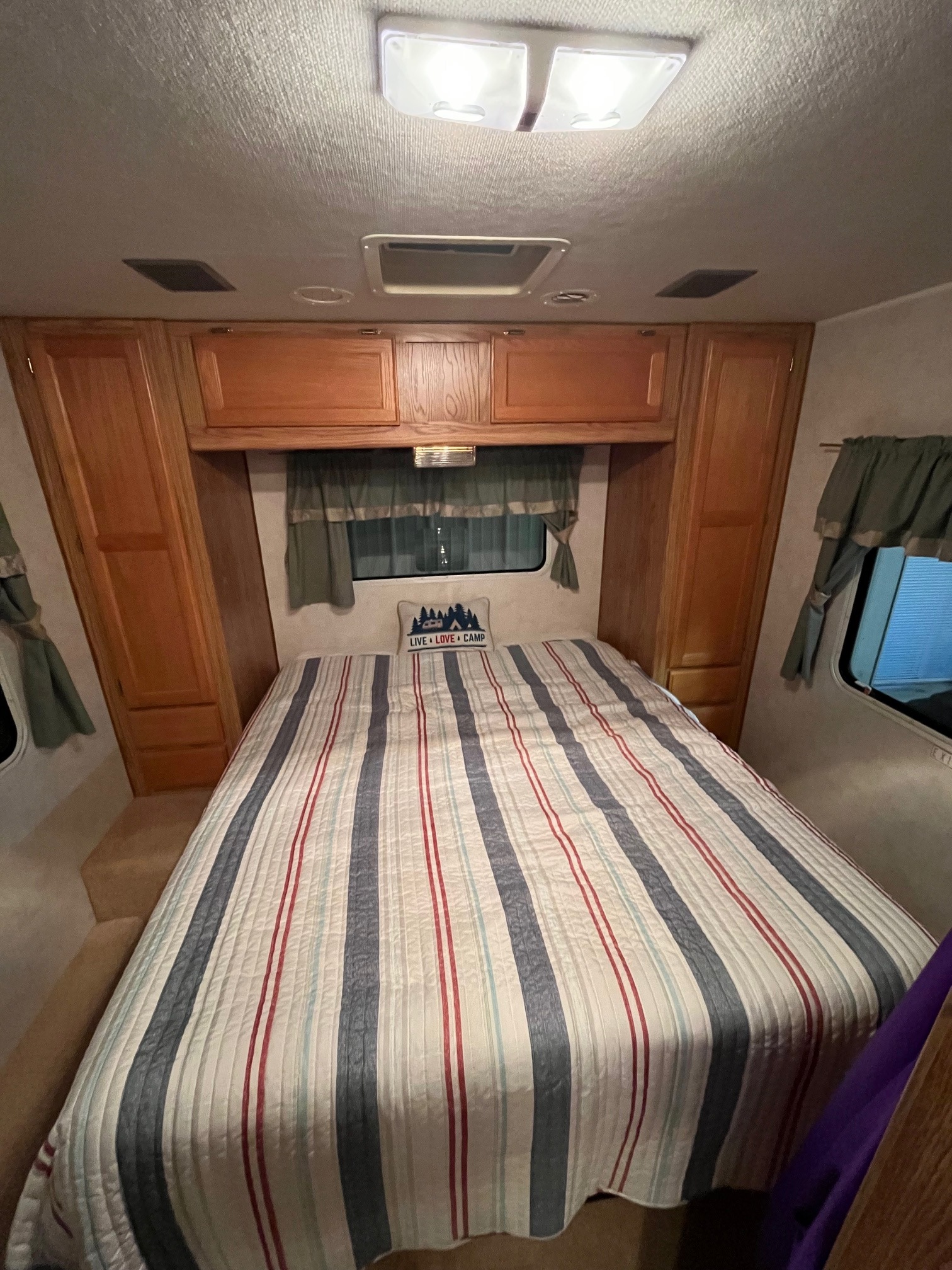 Cozy RV rental bedroom features a striped bed, wooden storage, and windows. Ideal for comfortable camping.. Gulf Stream Ultra Supreme 2002