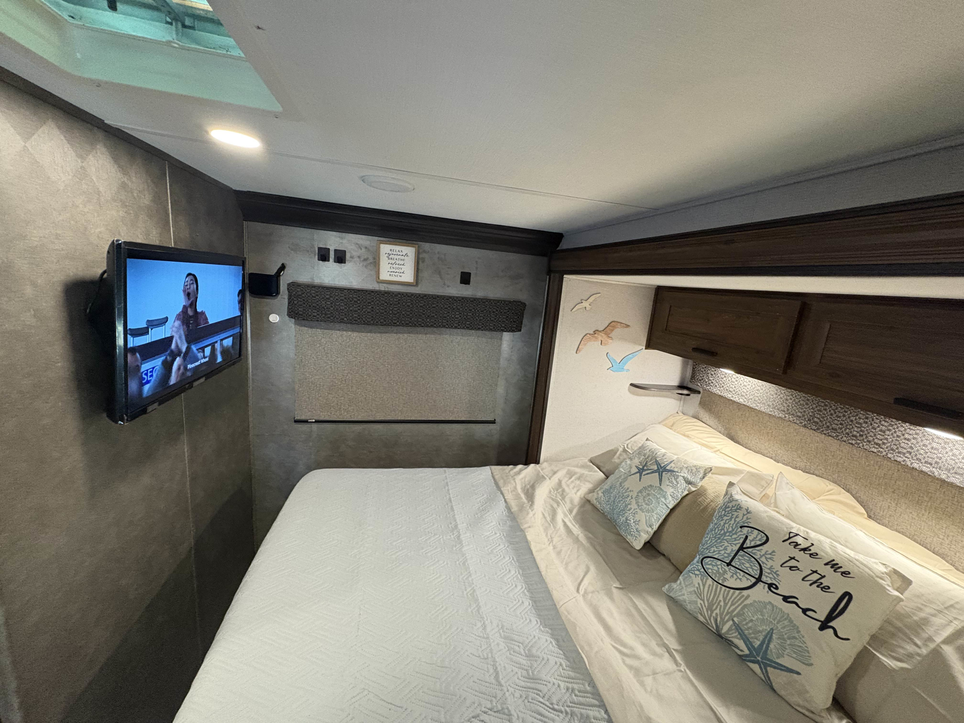 Comfortable RV rental bedroom, featuring a TV, bed with beach pillows, and window shade, offering a relaxing stay.. Forest River Sunseeker LE 2021