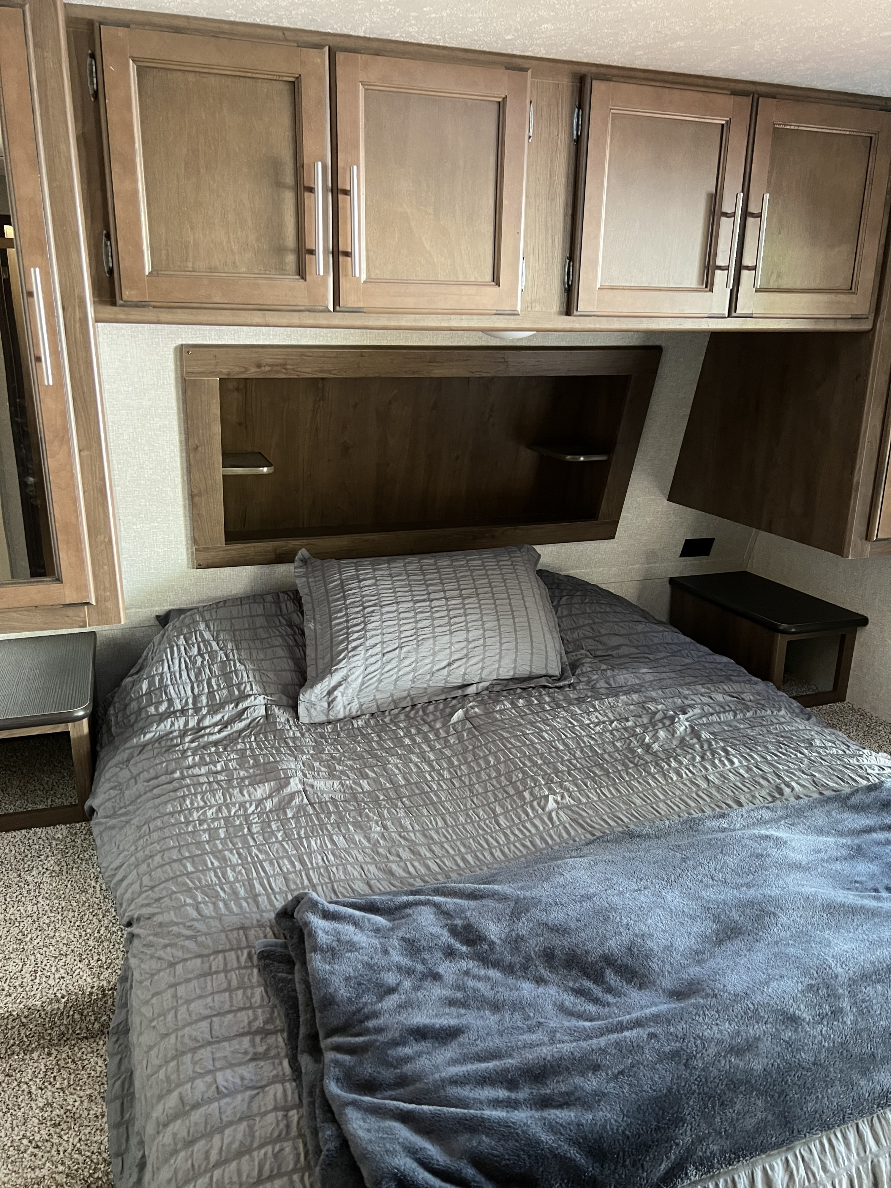 This RV rental bedroom features a cozy bed with grey bedding, overhead cabinets, and built-in storage for compact living.. Keystone RV Cougar 2018
