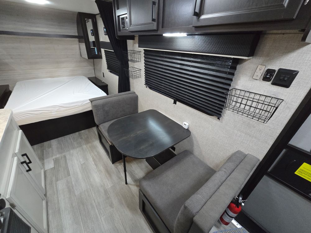 Modern rv rental interior: bed, dinette, kitchen cabinets, and safety items like a fire extinguisher. Light-toned finish.. Jayco Flight 195RB 2022