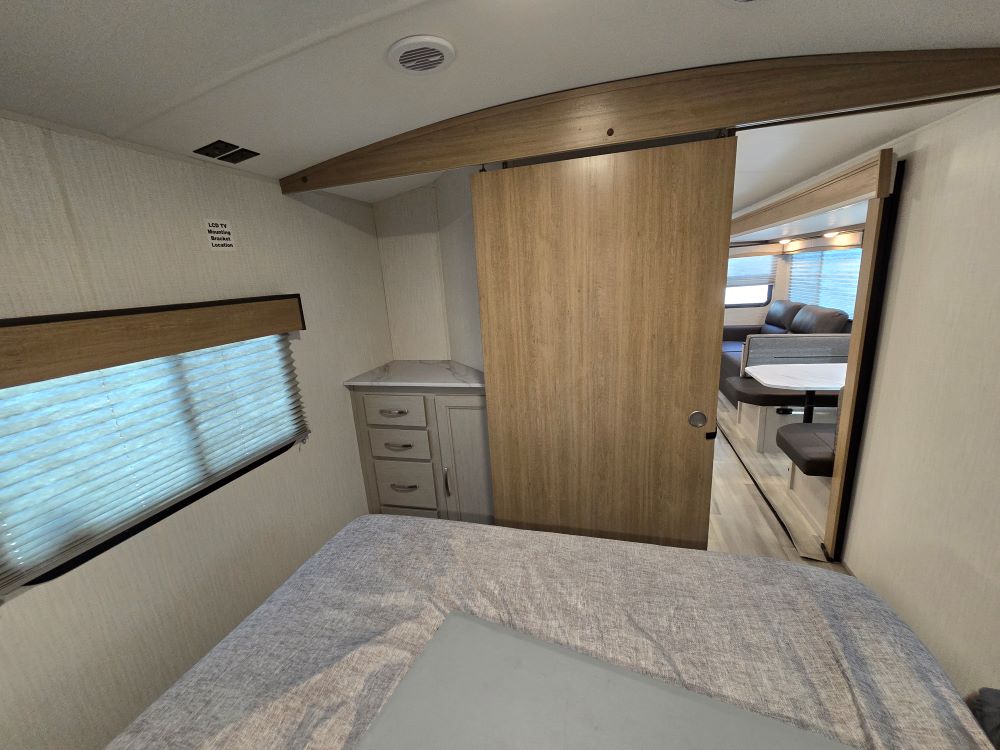 Explore the comfortable bedroom and living area inside this modern RV rental. Features a bed, dresser, and sliding door to the dinette.. Cruiser Embrace EL26RB 2024
