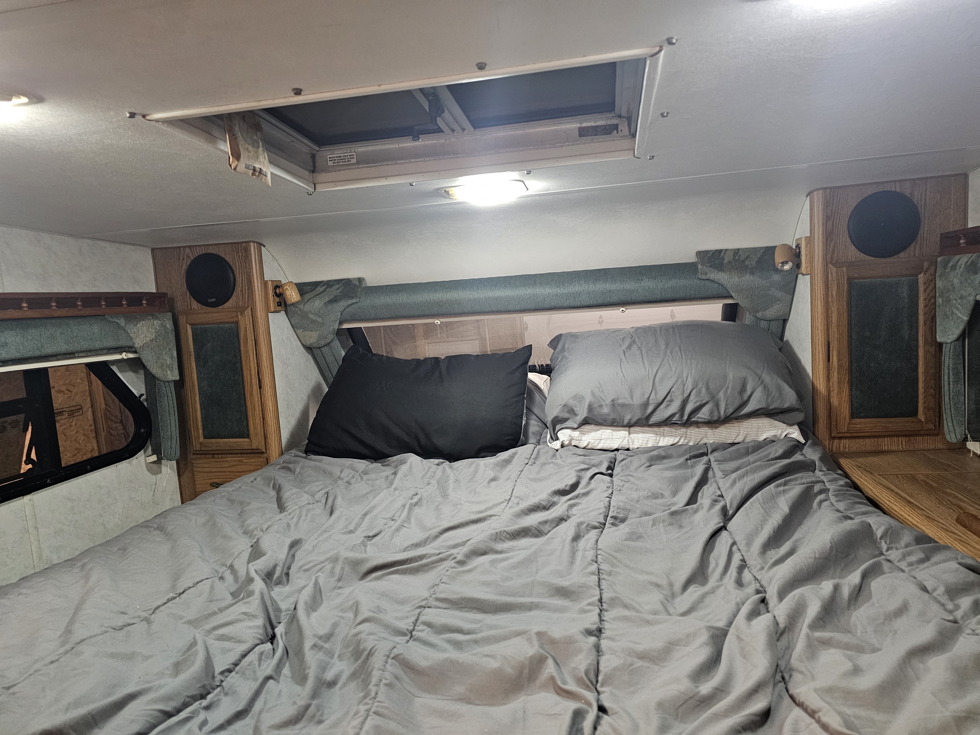 Comfortable RV rental bedroom interior. Features a grey bed, pillows, wooden cabinetry, and overhead vent for travel comfort.. Lance legend 880 2018
