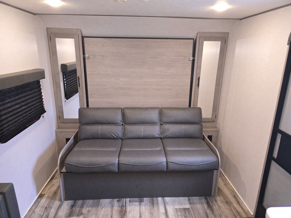 RV rental interior: Sofa lounge with a wall-mounted murphy bed above, flanked by practical storage cabinets.. Coleman 1855RB 2022
