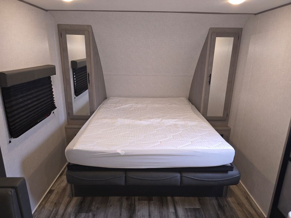 Spacious RV rental bedroom featuring a comfortable bed, built-in mirrored storage, and privacy blinds for your trip.. Coleman 1855RB 2022