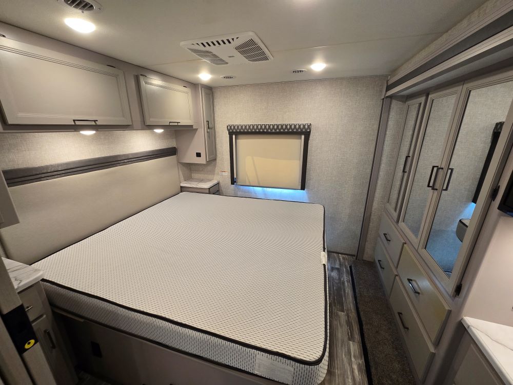 Comfortable RV rental bedroom featuring a large bed, overhead storage, and mirrored wardrobe for your travels.. Thor Hurricane 29M 2022