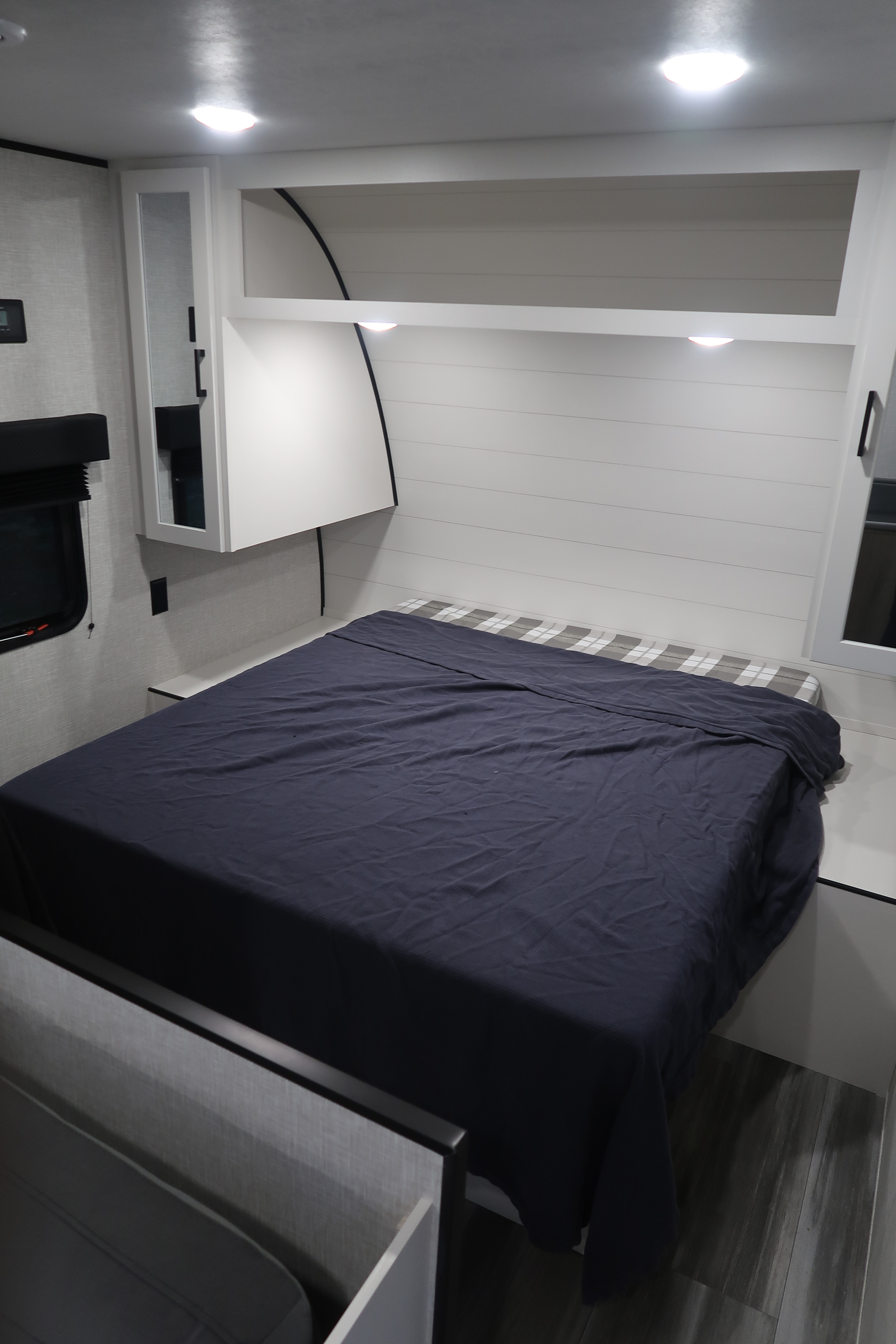 Spacious RV rental bedroom featuring a queen bed with dark blue bedding, overhead cabinets, and reading lights.. Jayco Jay Flight SLX 2025